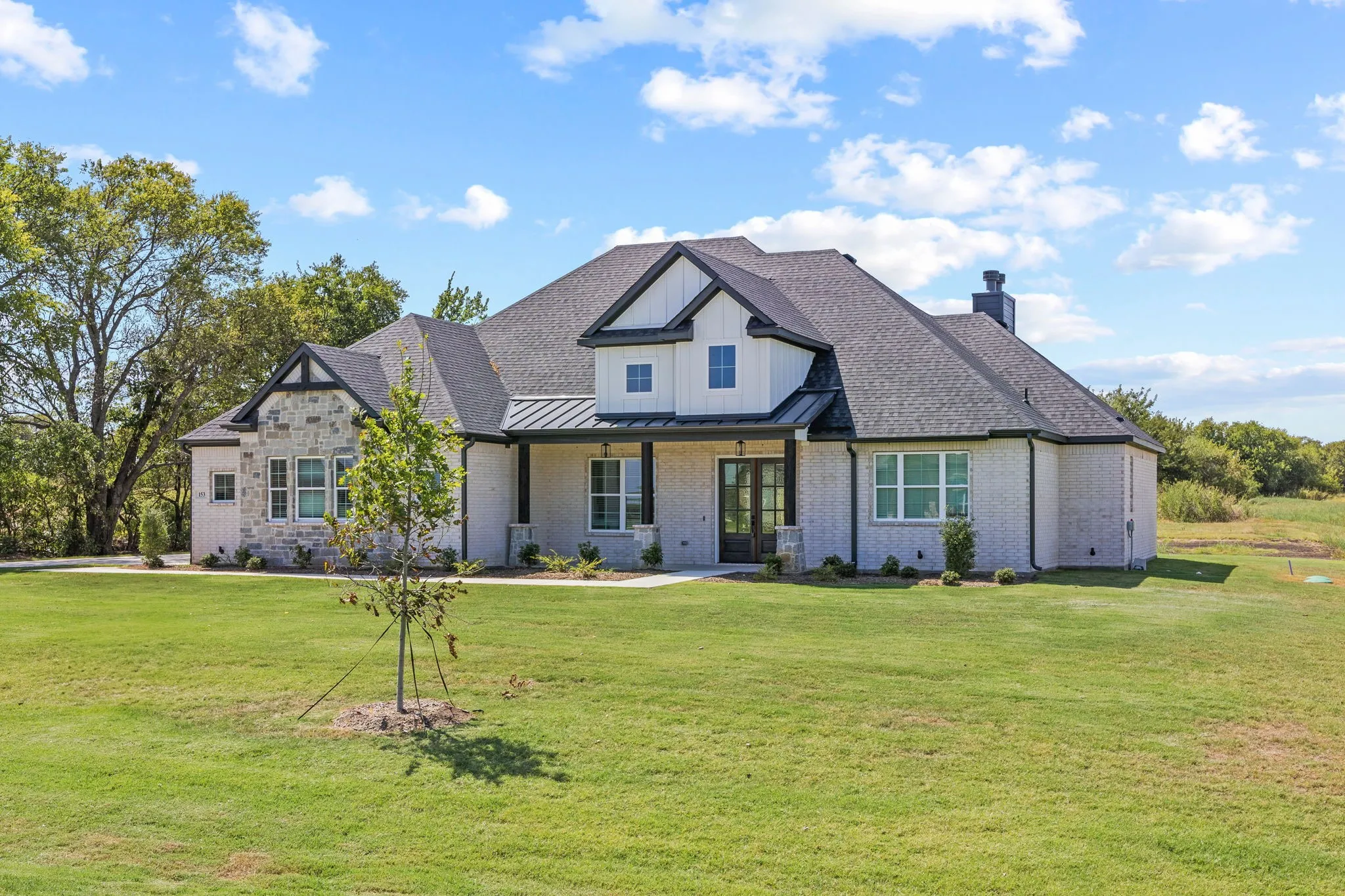 Exterior featuring a light brick facade, natural stone accents, a dark shingle roof, a covered entry, and a prominent chimney