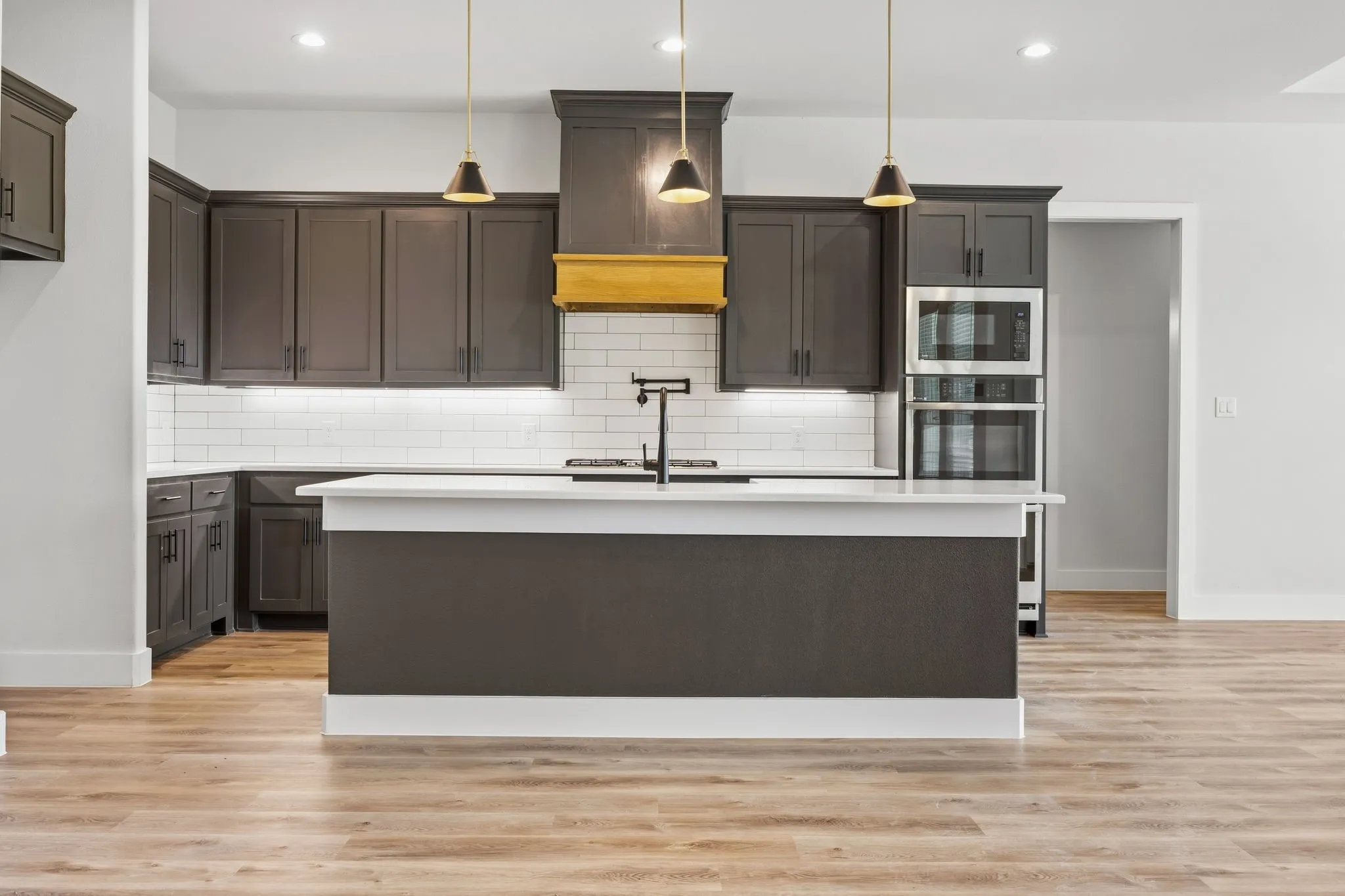 Contemporary kitchen featuring dark cabinetry, a central island with white countertop, subway tile backsplash, stainless steel double wall ovens, and wood-finish flooring