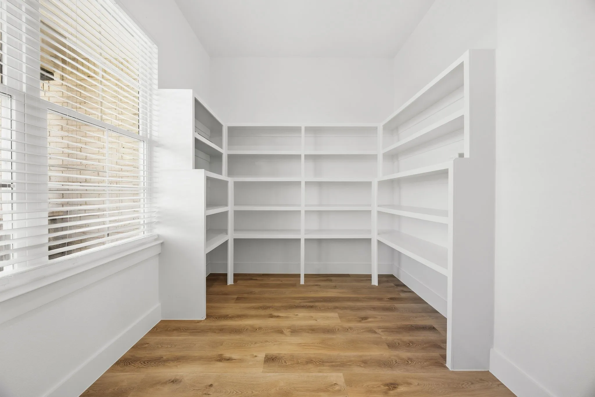 Built-in shelving, wood-finish flooring, white window blinds, and white trim