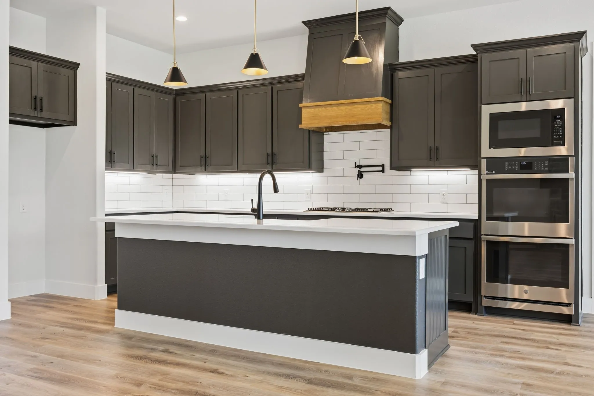 Kitchen featuring dark cabinetry, a center island with a white countertop, built-in stainless steel appliances, and wood-finish flooring