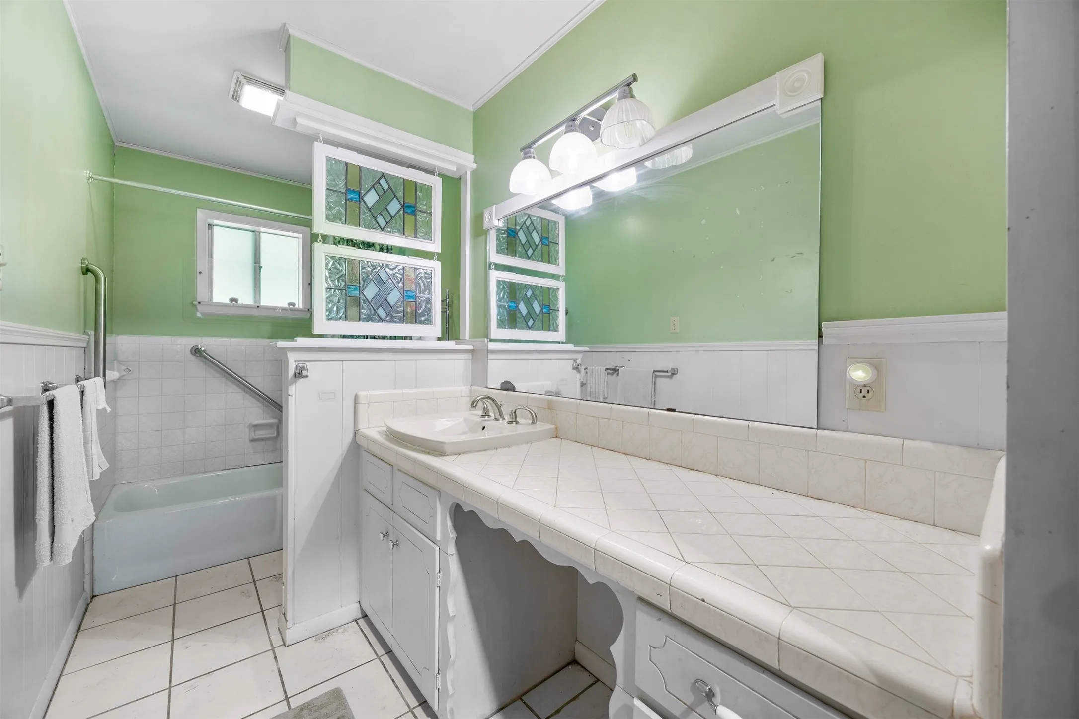 Bathroom featuring a built-in vanity with tiled countertop, single basin sink, and ample storage cabinetry