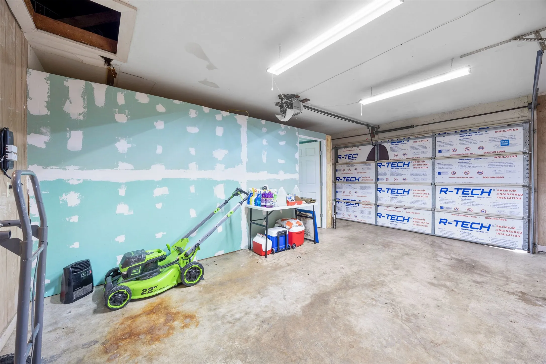 Attached single-car garage featuring a concrete floor, exposed insulation on the garage door, and a built-in access panel to the attic