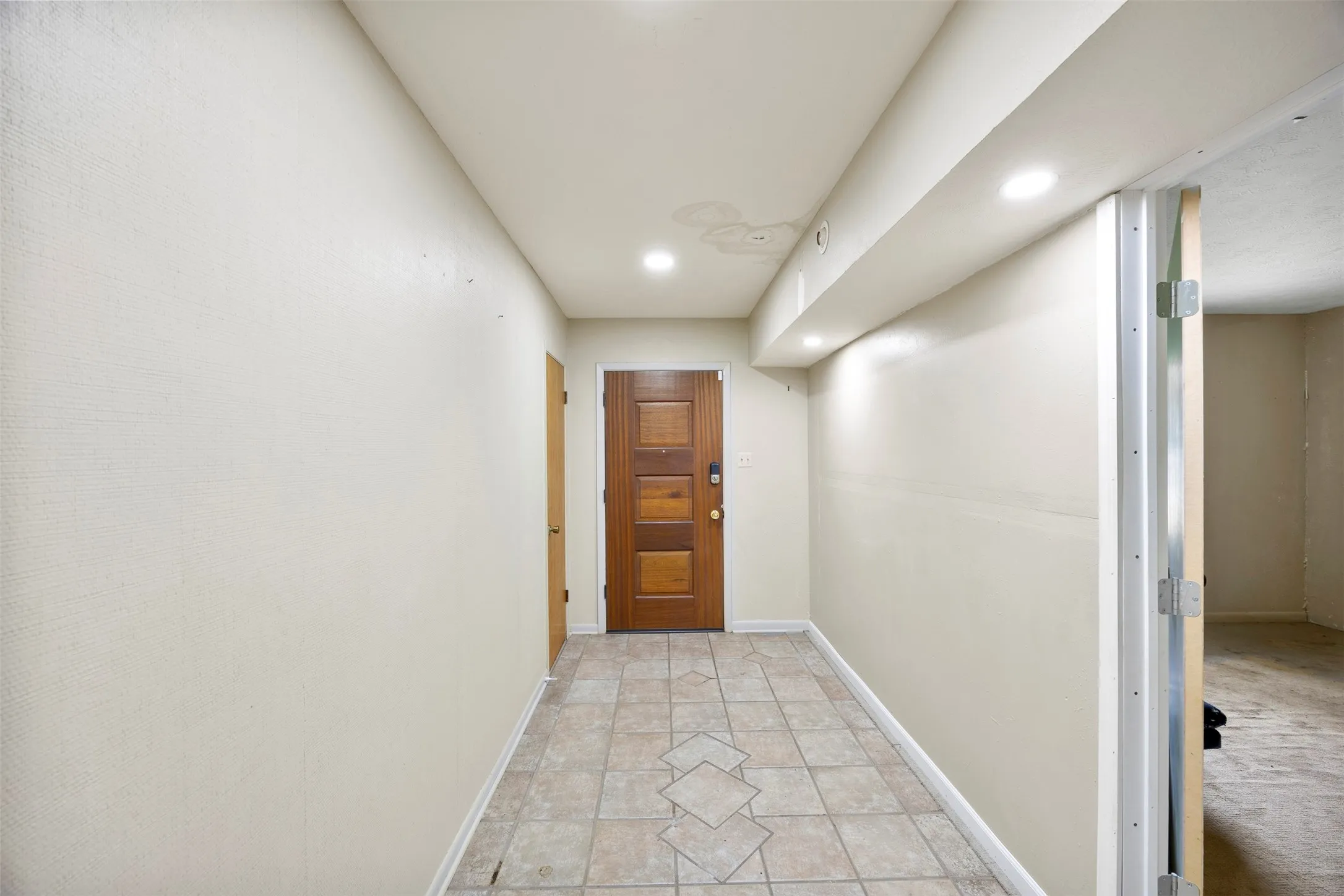 Entryway featuring a wood-panel door, neutral-toned walls, recessed lighting, and square tile flooring with a decorative inlay