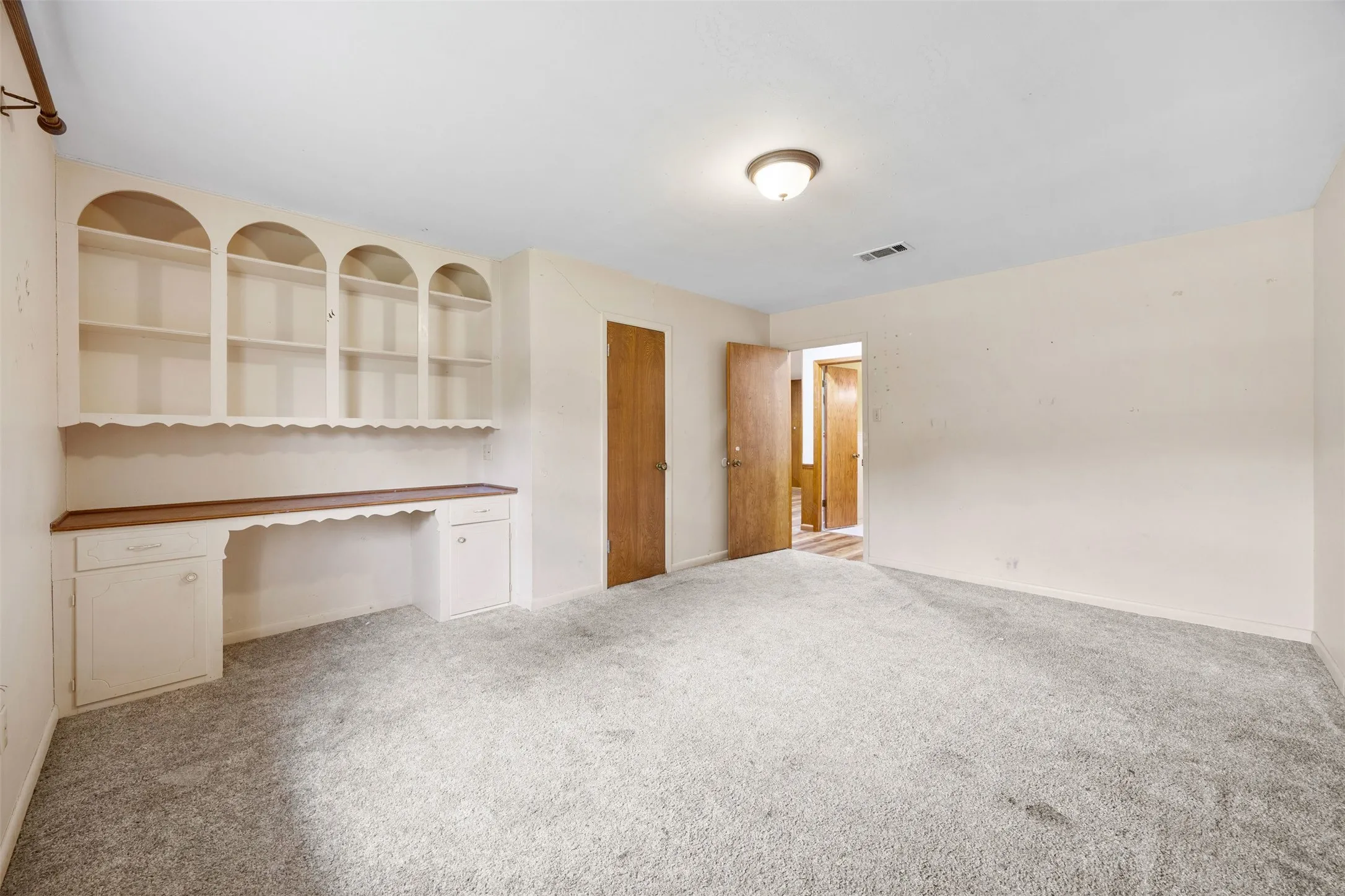 Built-in desk with arched shelving, light-toned walls, and grey carpet flooring
