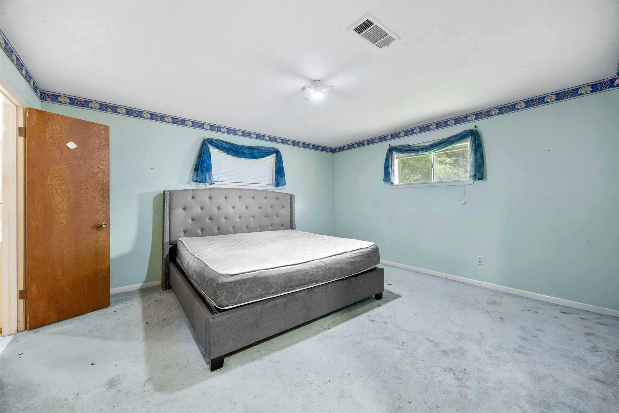 Light blue walls with a decorative border, light-colored carpeting, and a window with a sheer blue valance