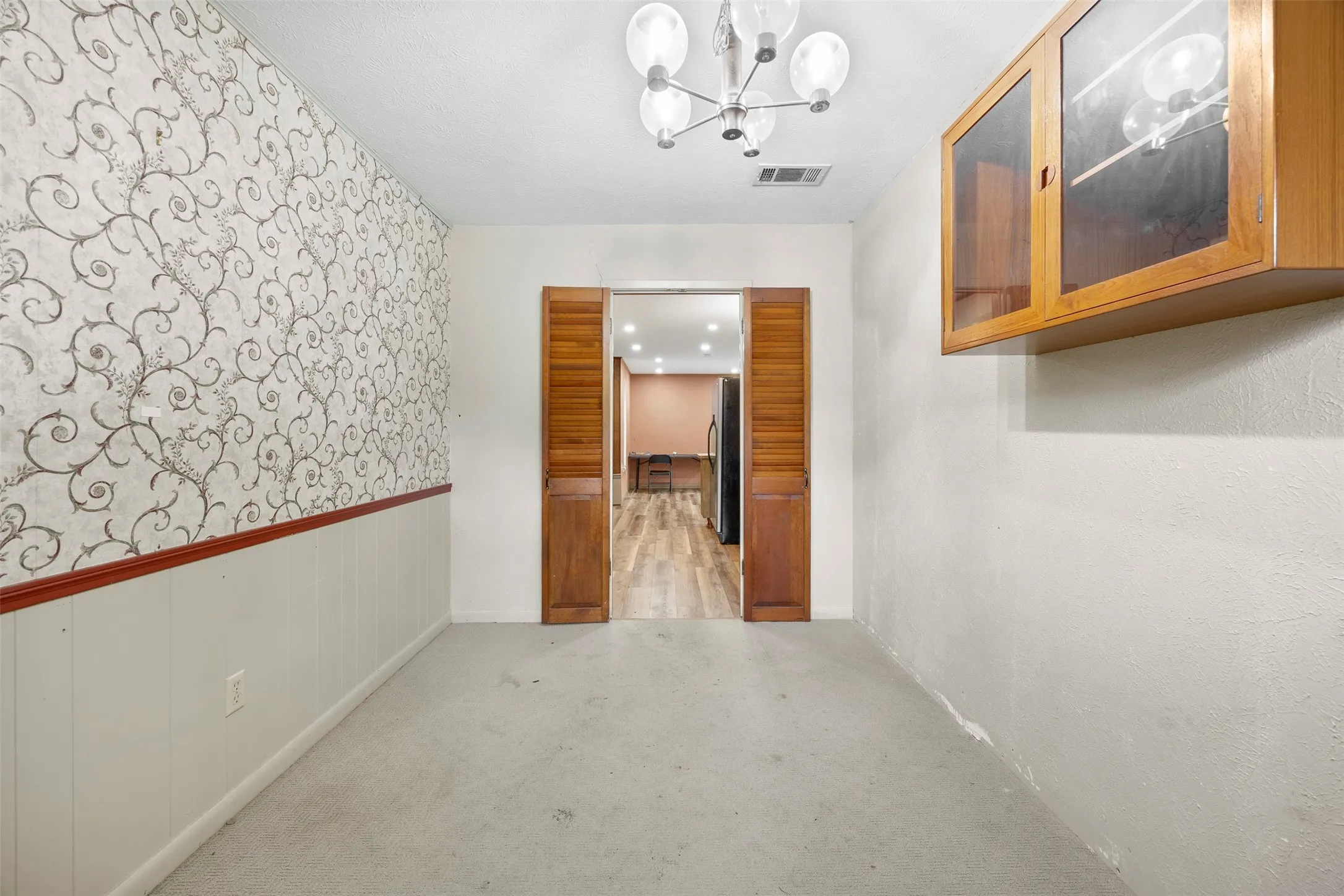 Room featuring a decorative wallpaper accent wall with chair rail molding and wainscoting