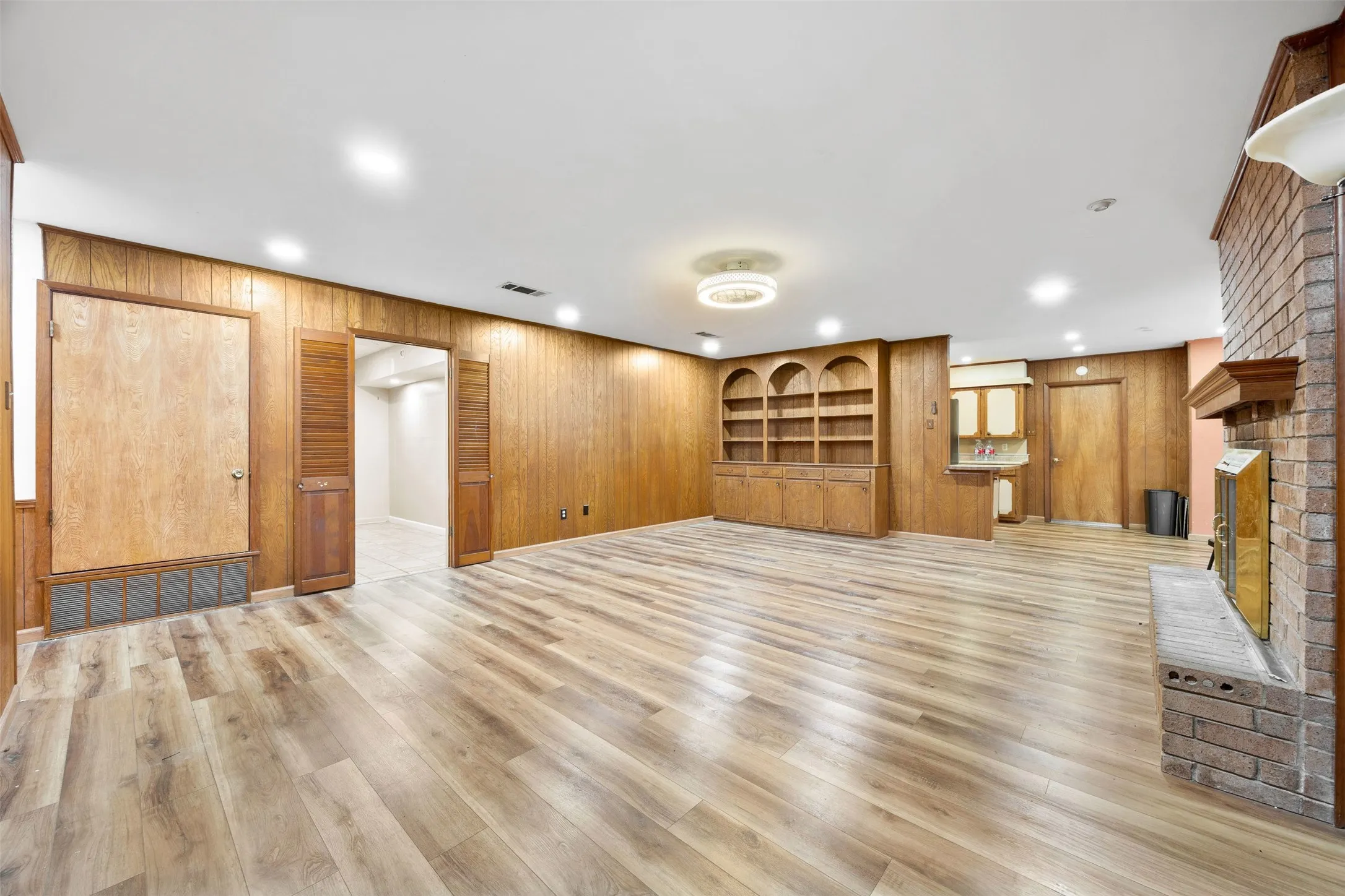 Spacious interior featuring wood-finish flooring, wood paneling, recessed lighting, built-in shelving, and a brick fireplace