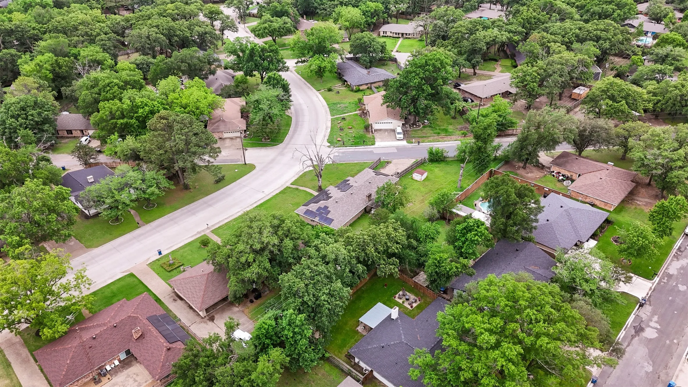 Residential neighborhood featuring mature trees, paved streets, and a mix of single-story homes