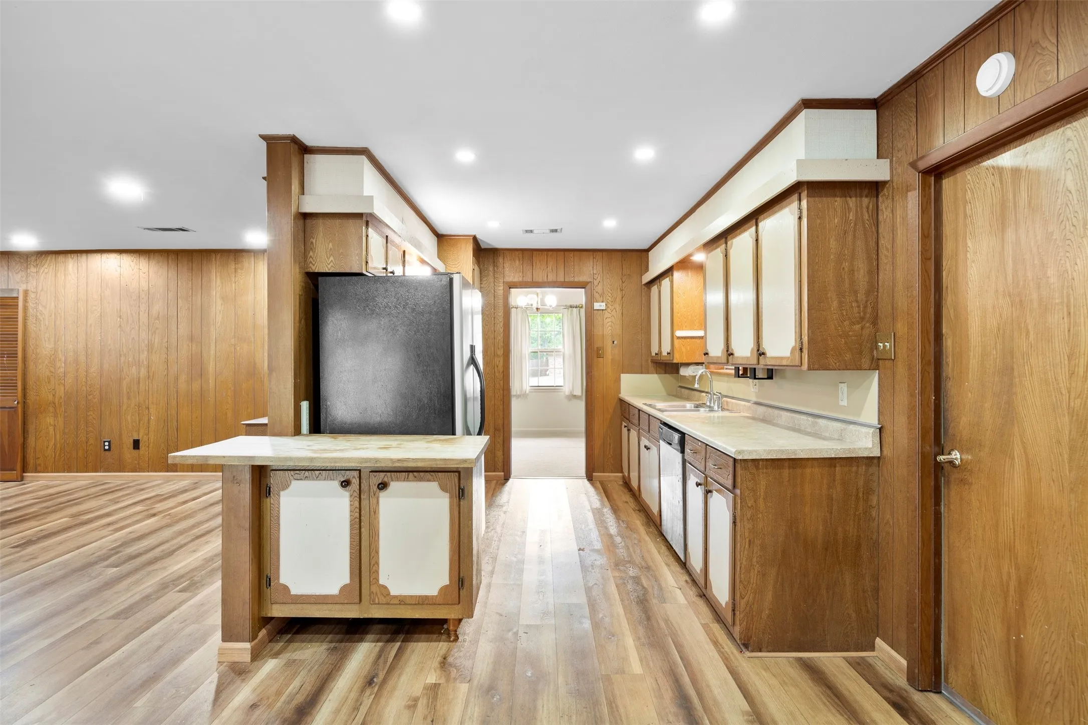 Open-concept kitchen with wood-finish flooring, recessed lighting, wood-paneled walls, and a built-in breakfast bar