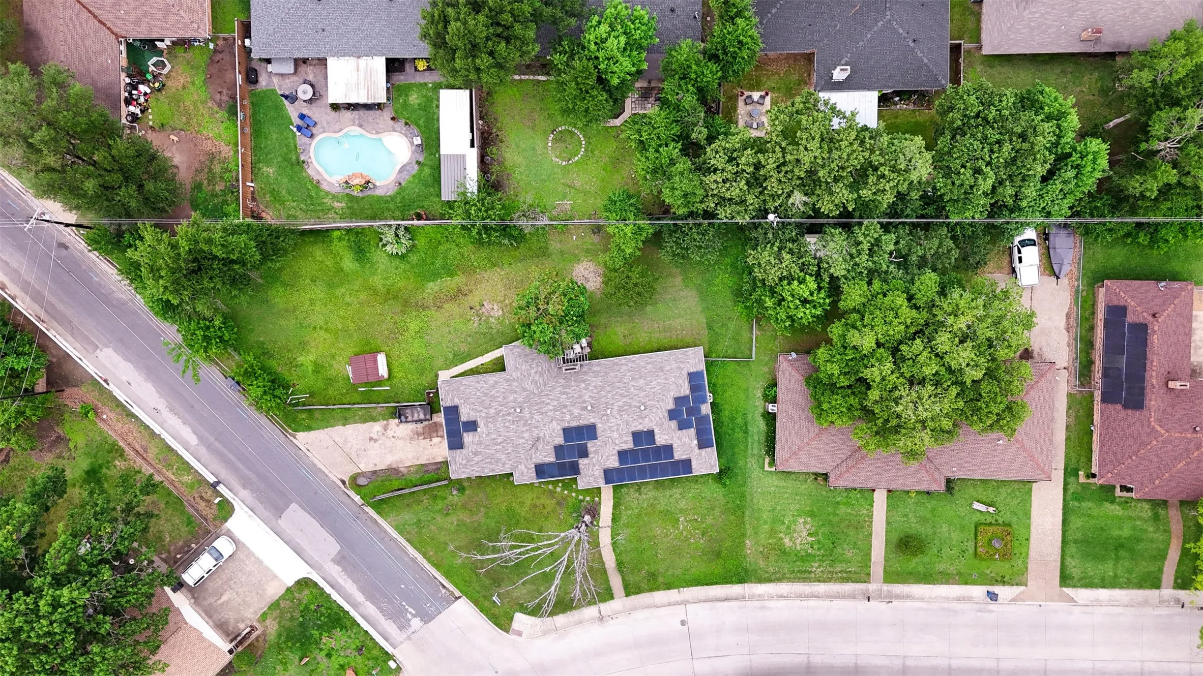 Aerial property view featuring a brown shingle roof with solar panels, a concrete driveway, and a grass lawn