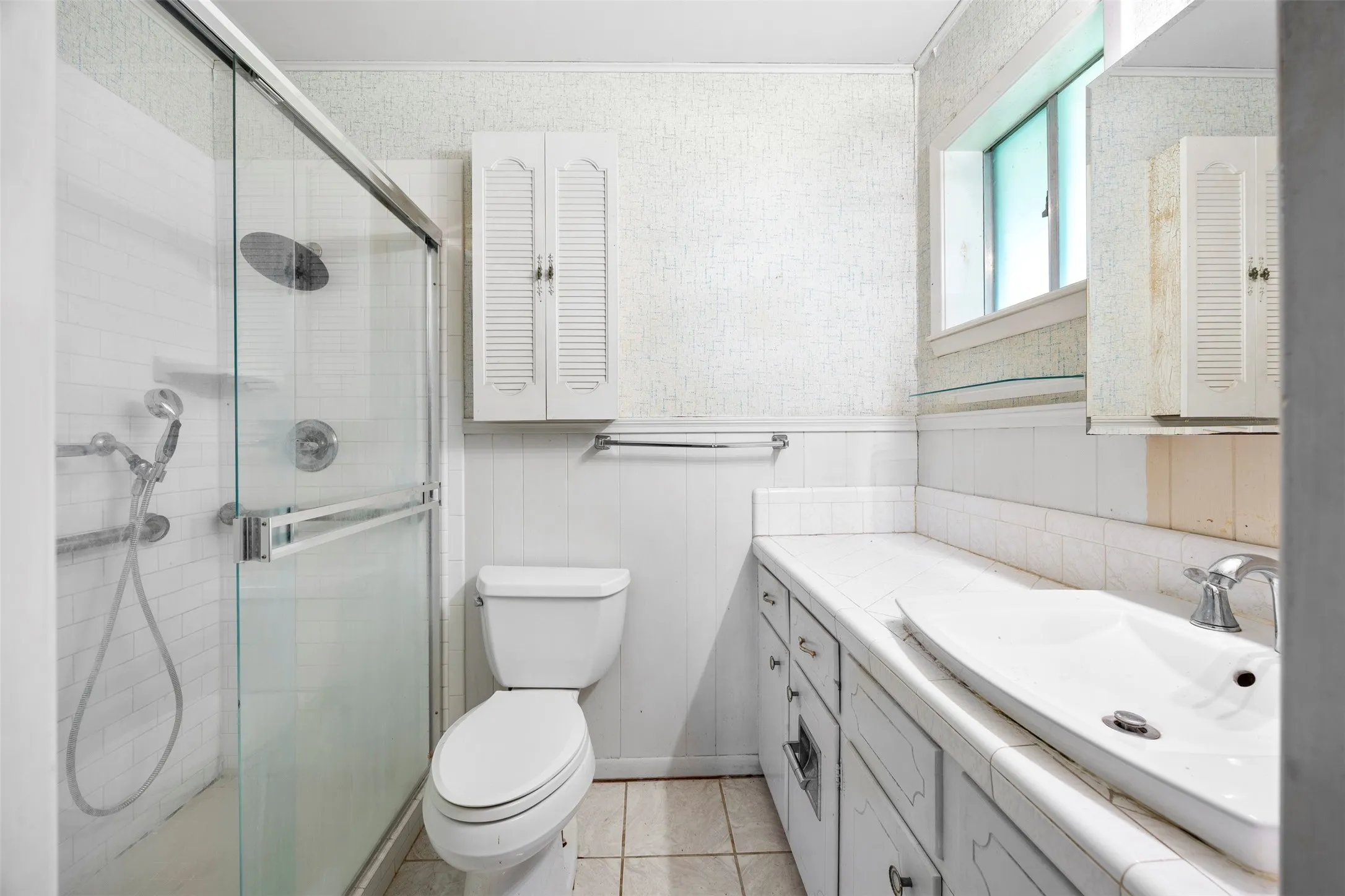 Full bathroom featuring a glass-enclosed shower with multiple showerheads, a vanity with an integrated sink, and white cabinetry