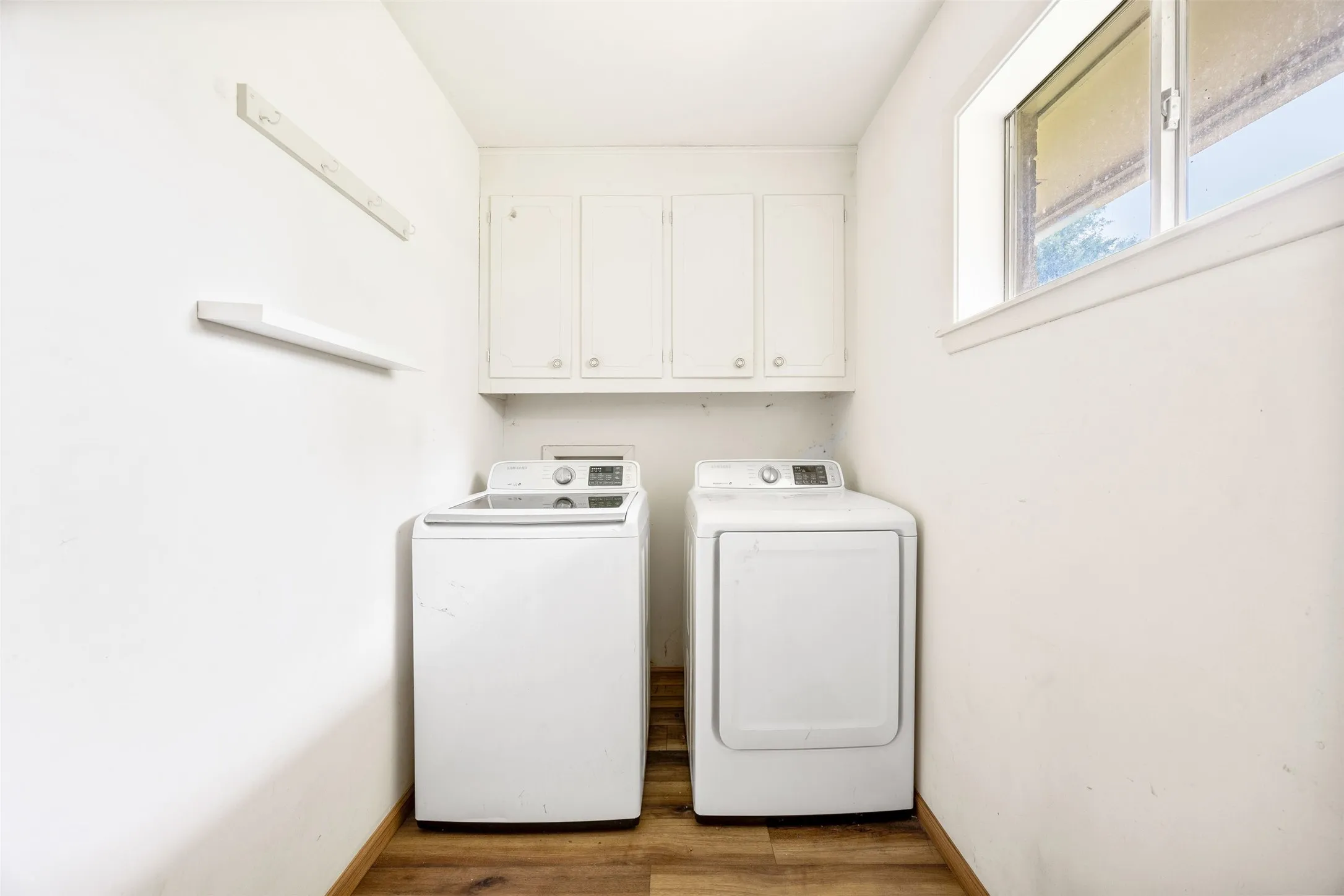 Dedicated laundry space featuring wood-finish flooring, white cabinetry, a built-in shelf, and an aluminum frame window
