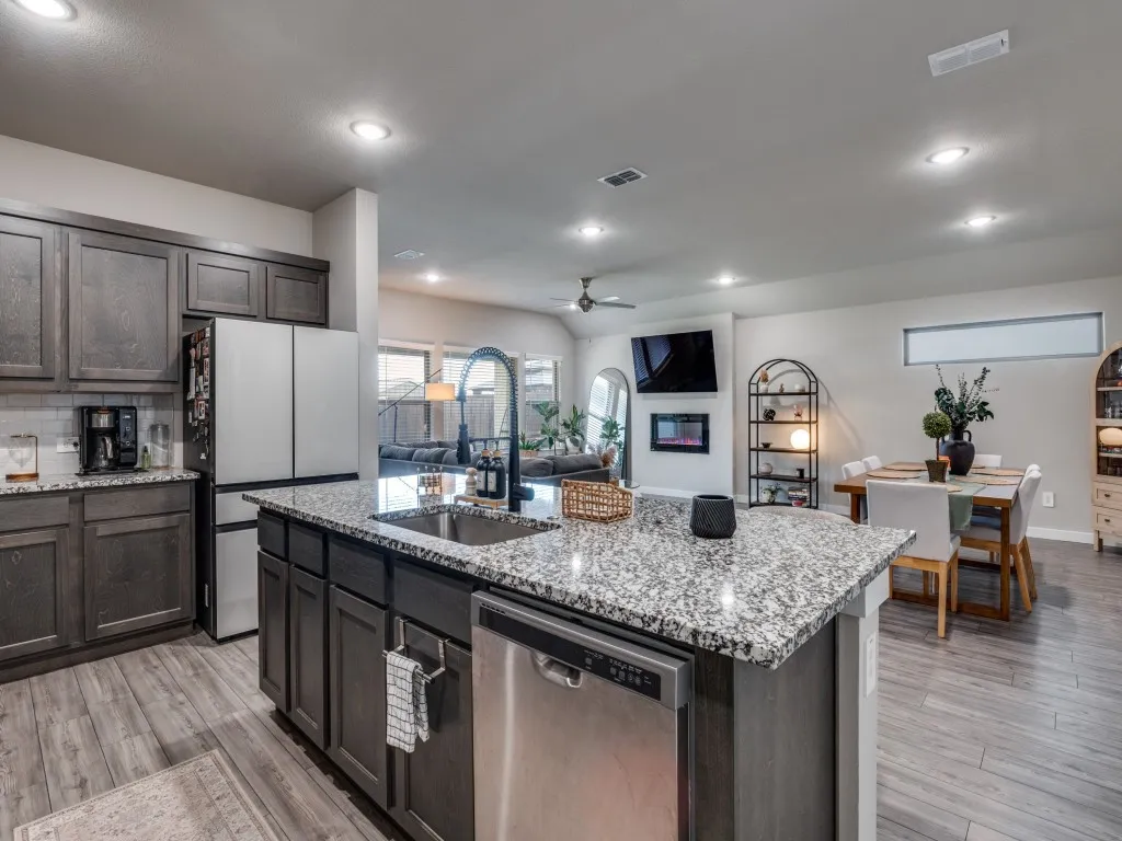 Modern kitchen featuring a granite-topped island with an undermount sink and gooseneck faucet, dark wood-finish cabinetry, stainless steel appliances, recessed lighting, and wood-finish flooring
