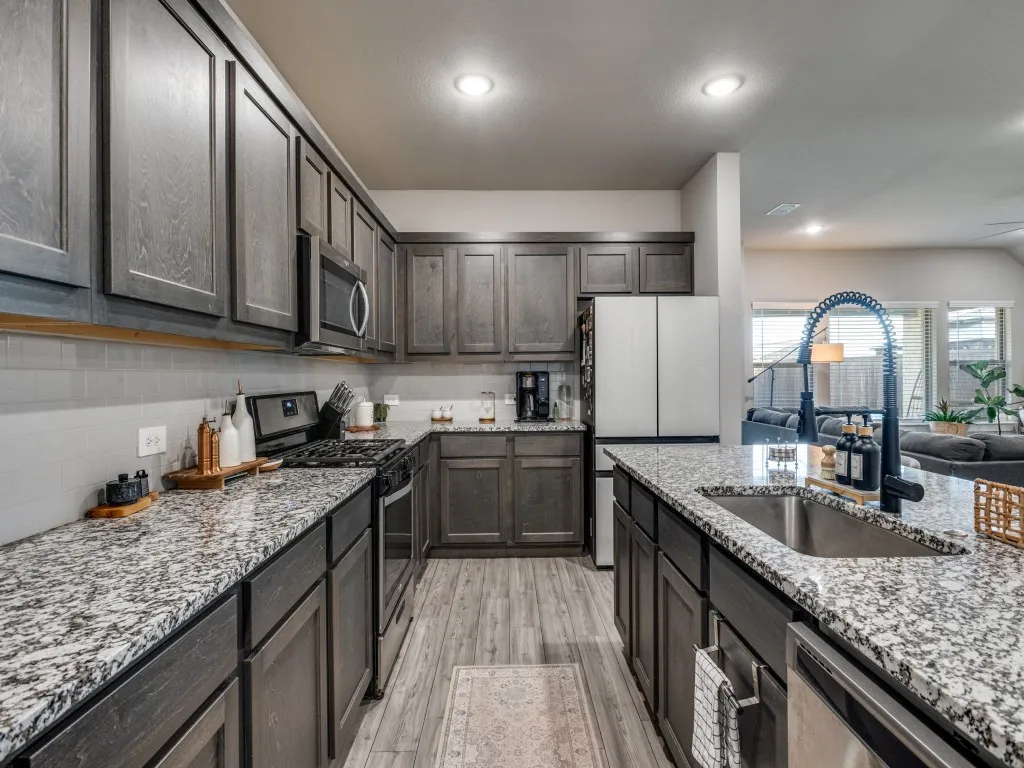 Contemporary kitchen featuring dark wood-finish cabinetry, speckled countertops, stainless steel appliances, a tile backsplash, and wood-finish flooring