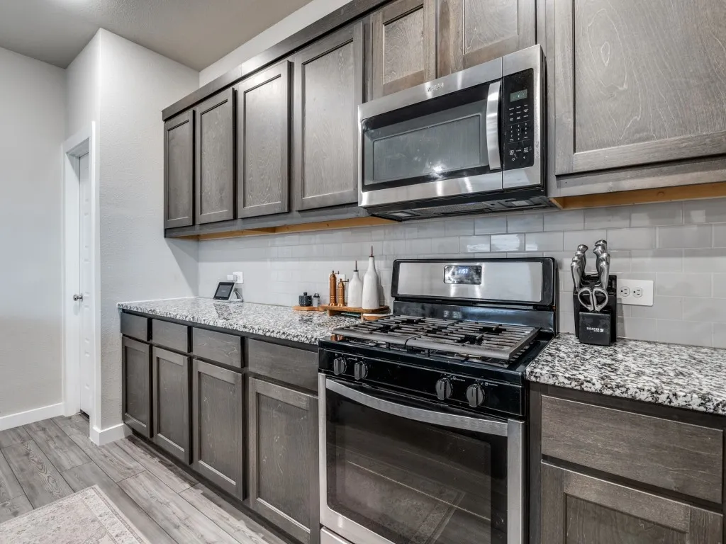 Kitchen featuring wood-finish cabinetry, granite-style countertops, stainless steel appliances, a gas range, and a subway tile backsplash