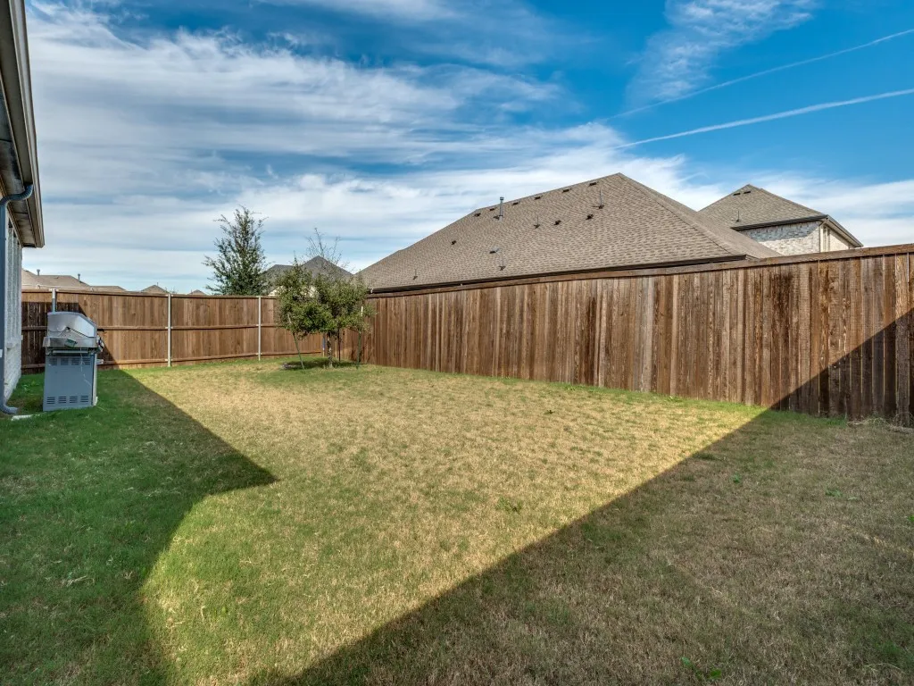 Spacious backyard featuring a full wood privacy fence and a young tree