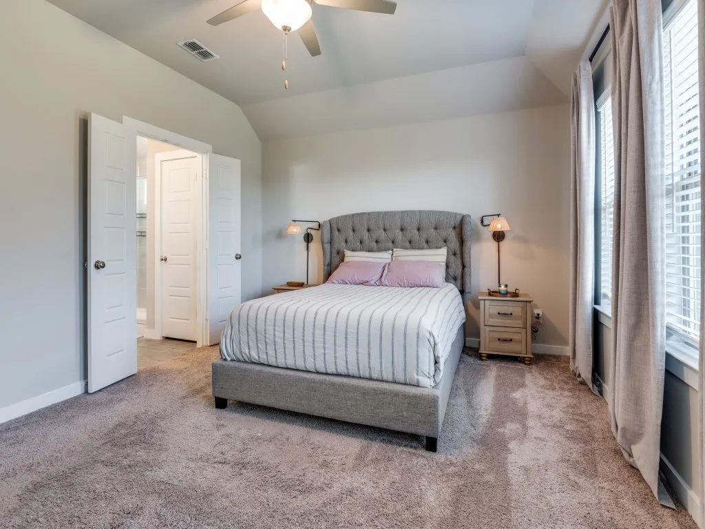 Carpeted bedroom featuring a vaulted ceiling with a fan light fixture, white interior doors, and a window with blinds