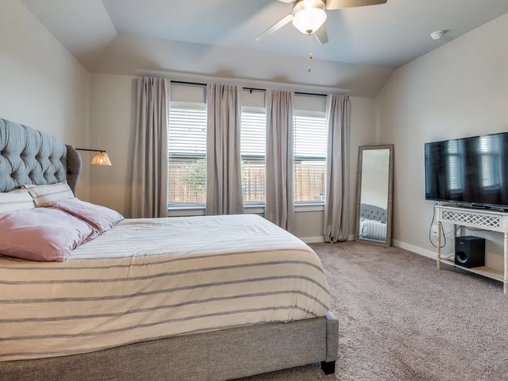 Bedroom featuring tray ceiling, ceiling fan with light fixture, three windows with blinds and curtain rods, recessed wall lighting, and plush carpet flooring