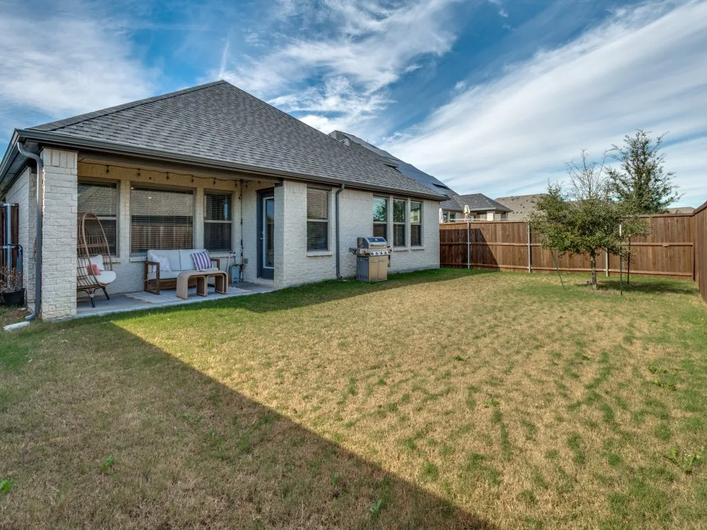 Expansive backyard featuring a partially covered patio, brick exterior, dark composition shingle roof, and a wood privacy fence