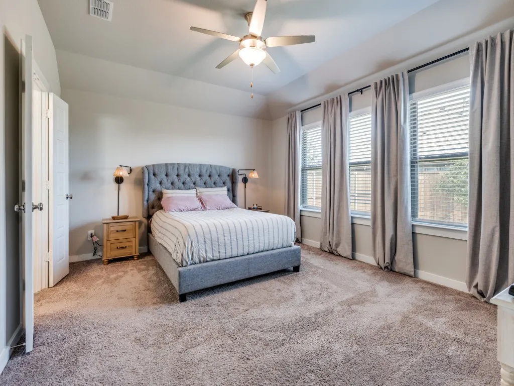Carpeted room featuring a ceiling fan with light, multiple windows with blinds and drapery, and a white paneled door