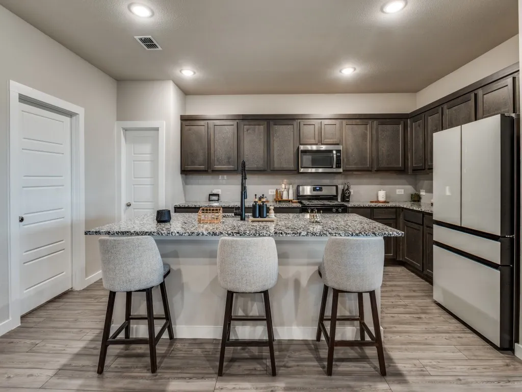 Kitchen featuring a spacious island with a light-toned countertop, dark wood cabinetry, stainless steel appliances, recessed lighting, and wood-finish flooring