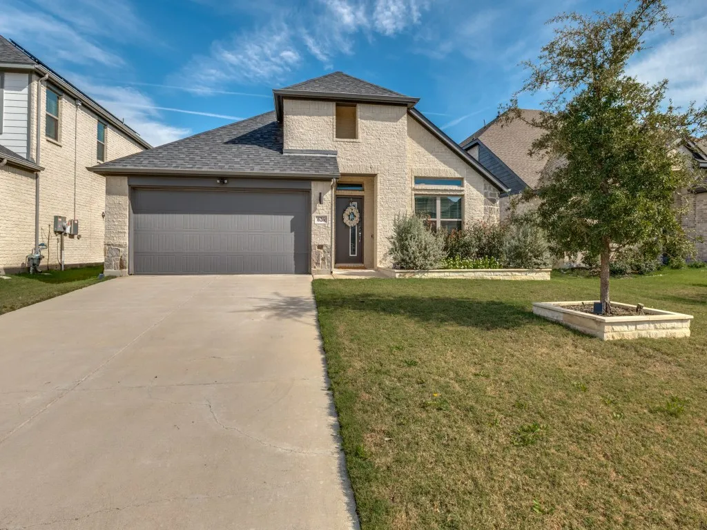 Front exterior showcasing a light-colored brick facade with stone accents, a dark gray garage door, and a concrete driveway