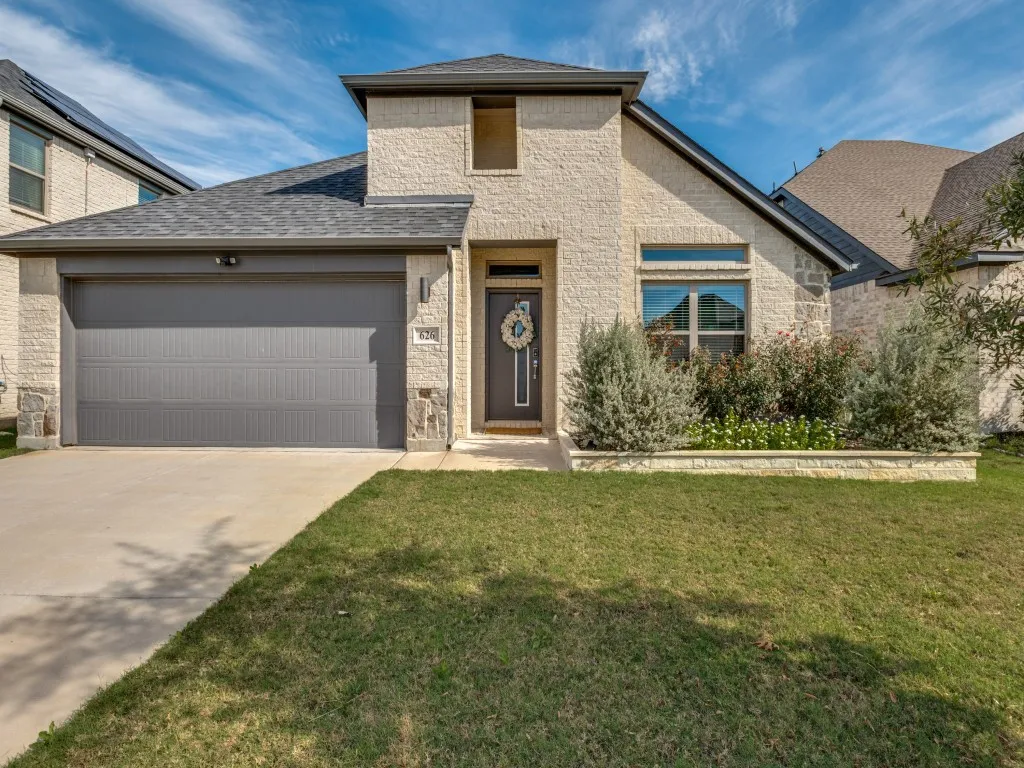 Stone and brick veneer facade with a dark gray garage door, a prominent arched window feature, and a paved driveway