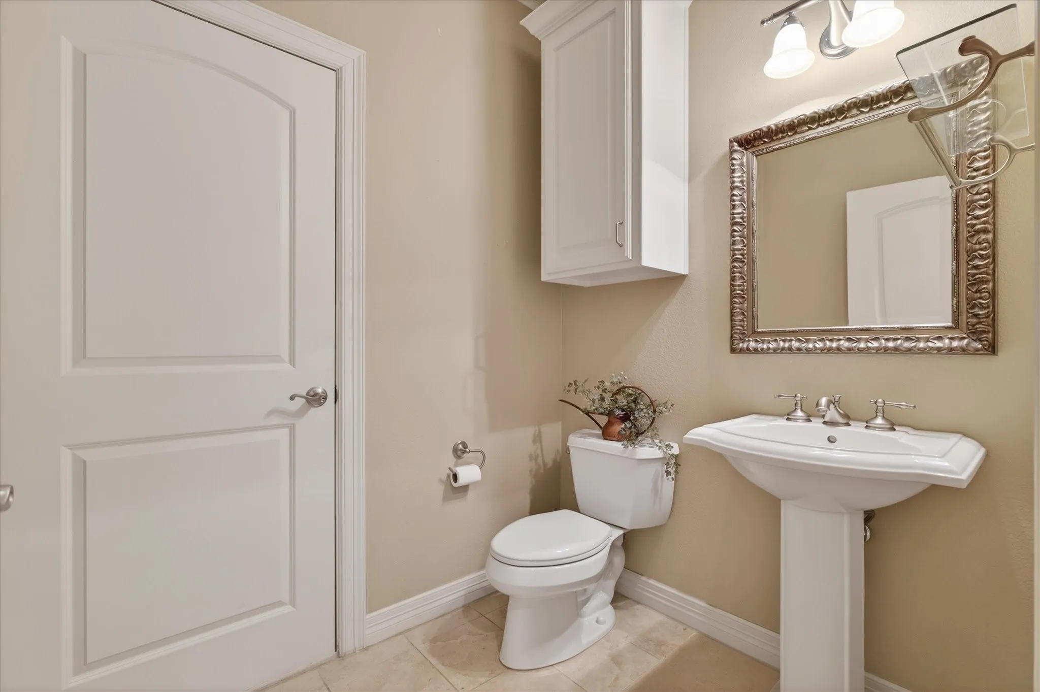 Pedestal sink with chrome fixtures, ornate framed mirror, and a wall-mounted vanity light