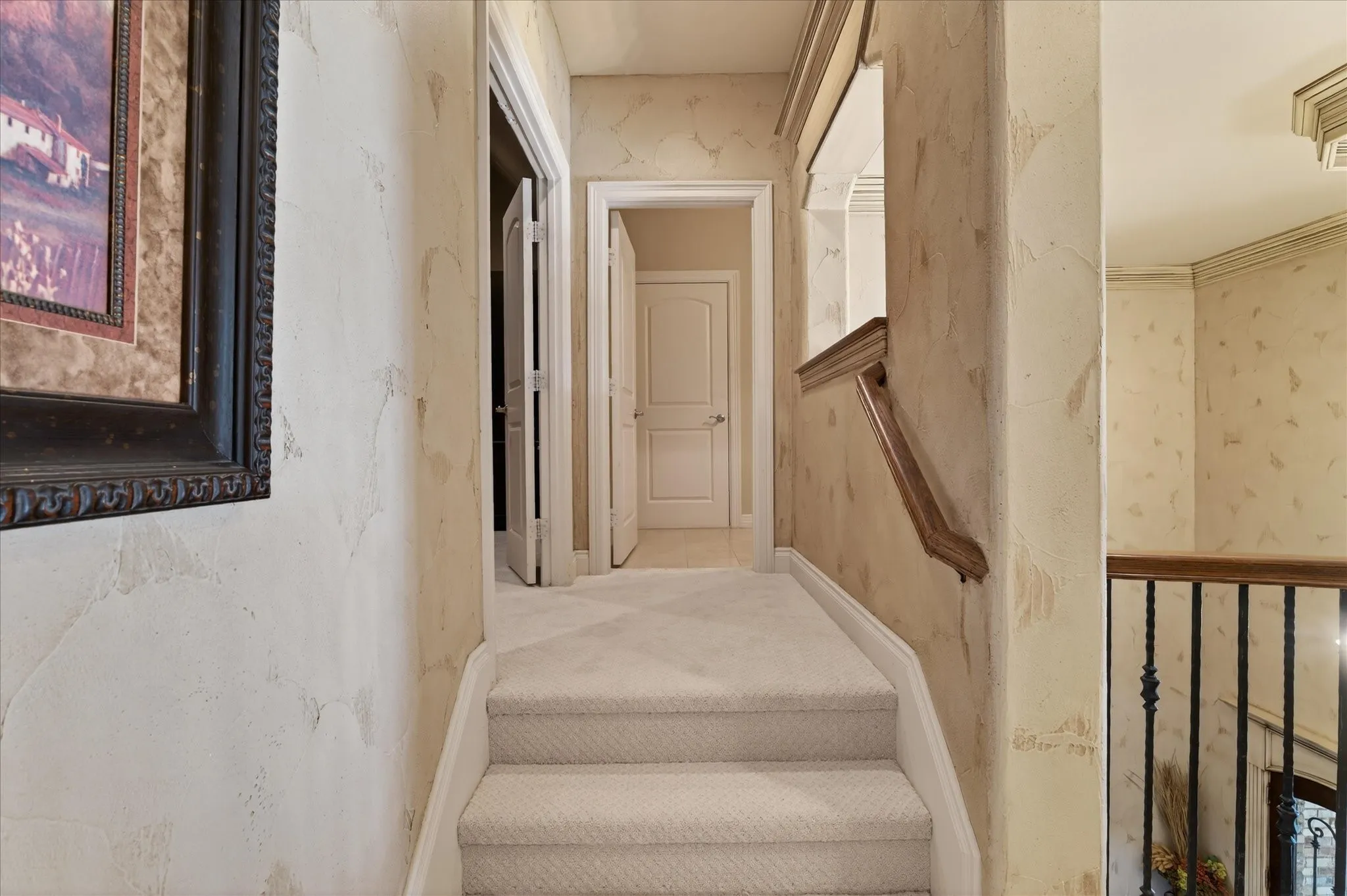 Carpeted staircase featuring white risers and handrail, textured wall finishes, and a decorative wrought iron baluster