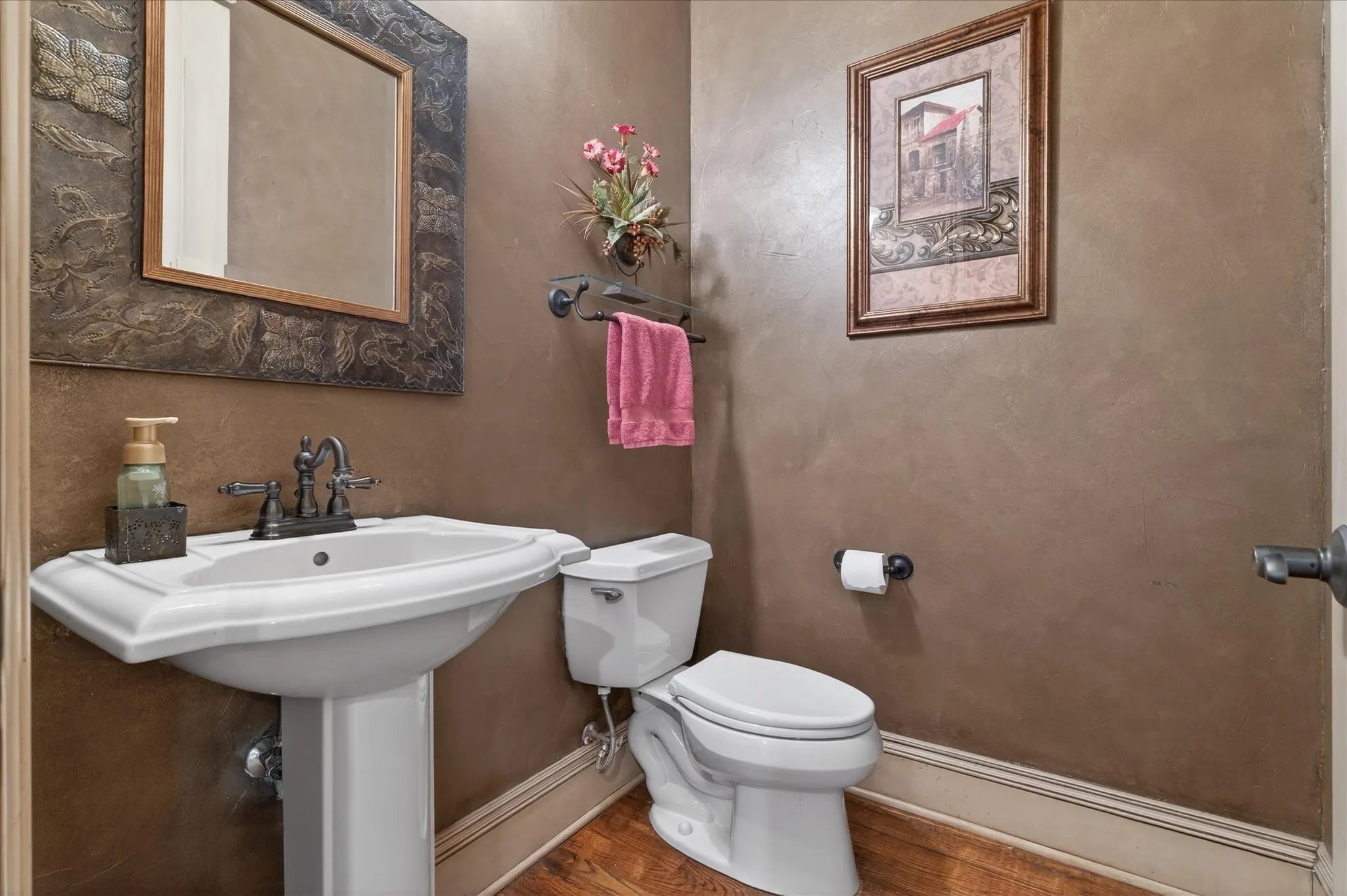 Pedestal sink with dark bronze faucet, framed mirror, and wood-finish flooring