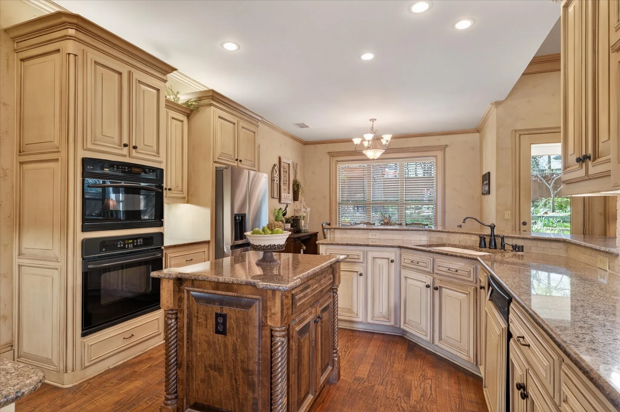Kitchen featuring a central island with granite countertop, wood-finish flooring, built-in double ovens, and extensive cabinetry with crown molding