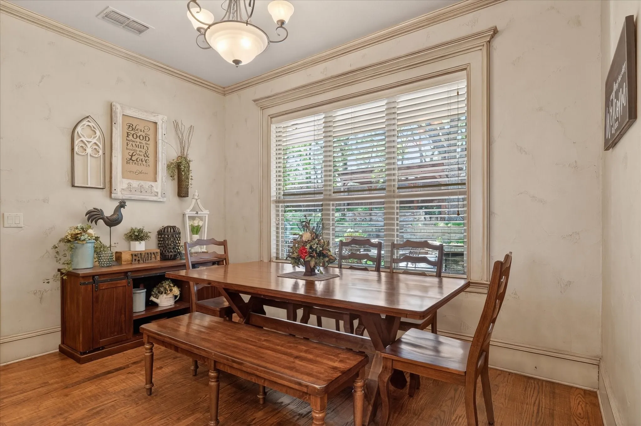Dining area featuring wood-finish flooring, a large window with horizontal blinds, decorative wall molding, and a ceiling-mounted light fixture