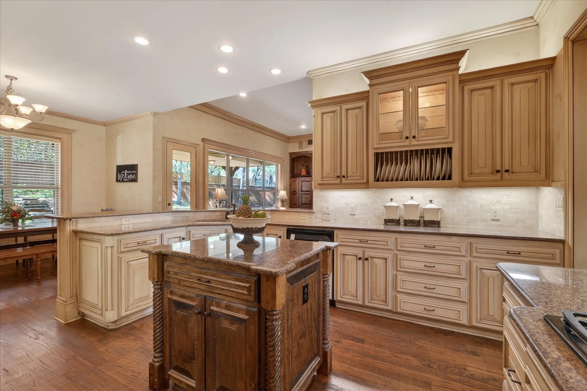Spacious kitchen featuring custom cabinetry, a built-in plate rack, under-cabinet lighting, wood-finish flooring, and a central island with a stone countertop
