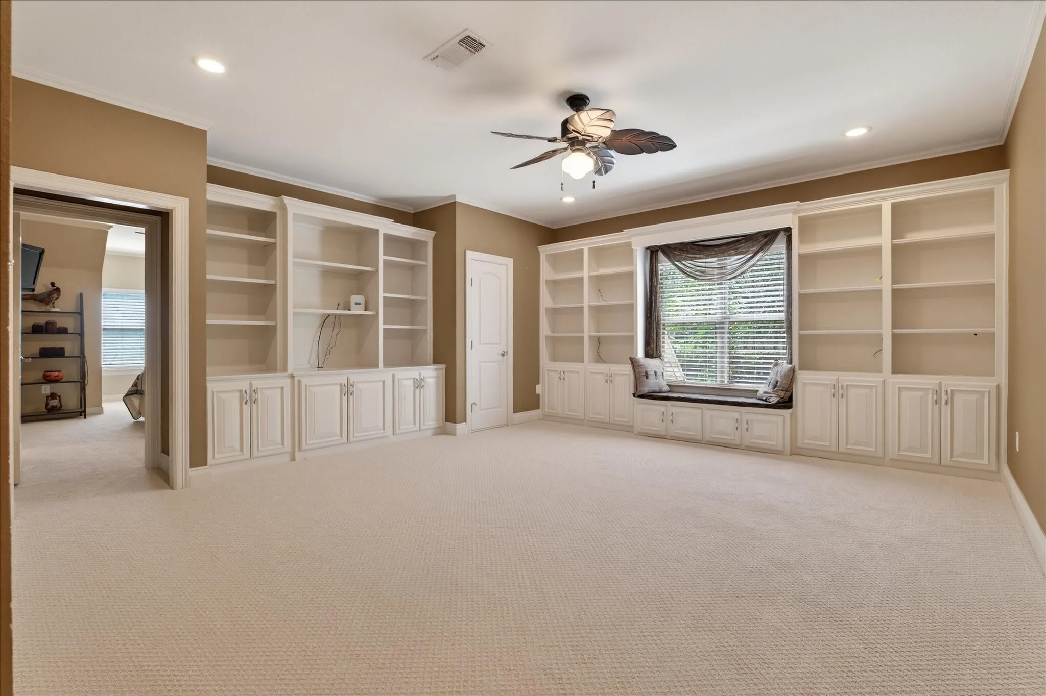 Spacious room featuring extensive built-in white cabinetry, a window seat with storage, recessed lighting, and a ceiling fan