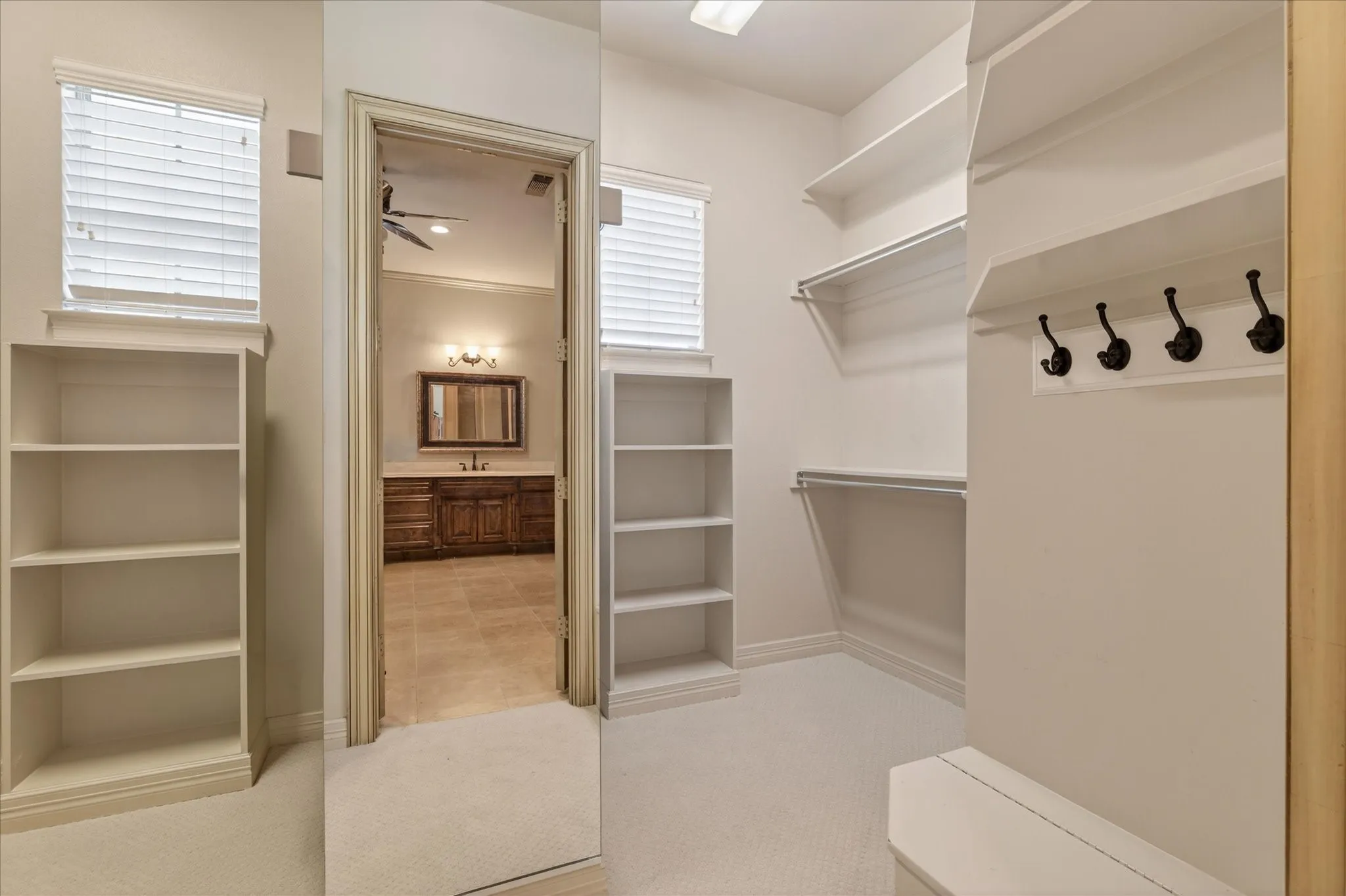 Walk-in closet featuring white shelving, hanging rods, an integrated bench, and coat hooks