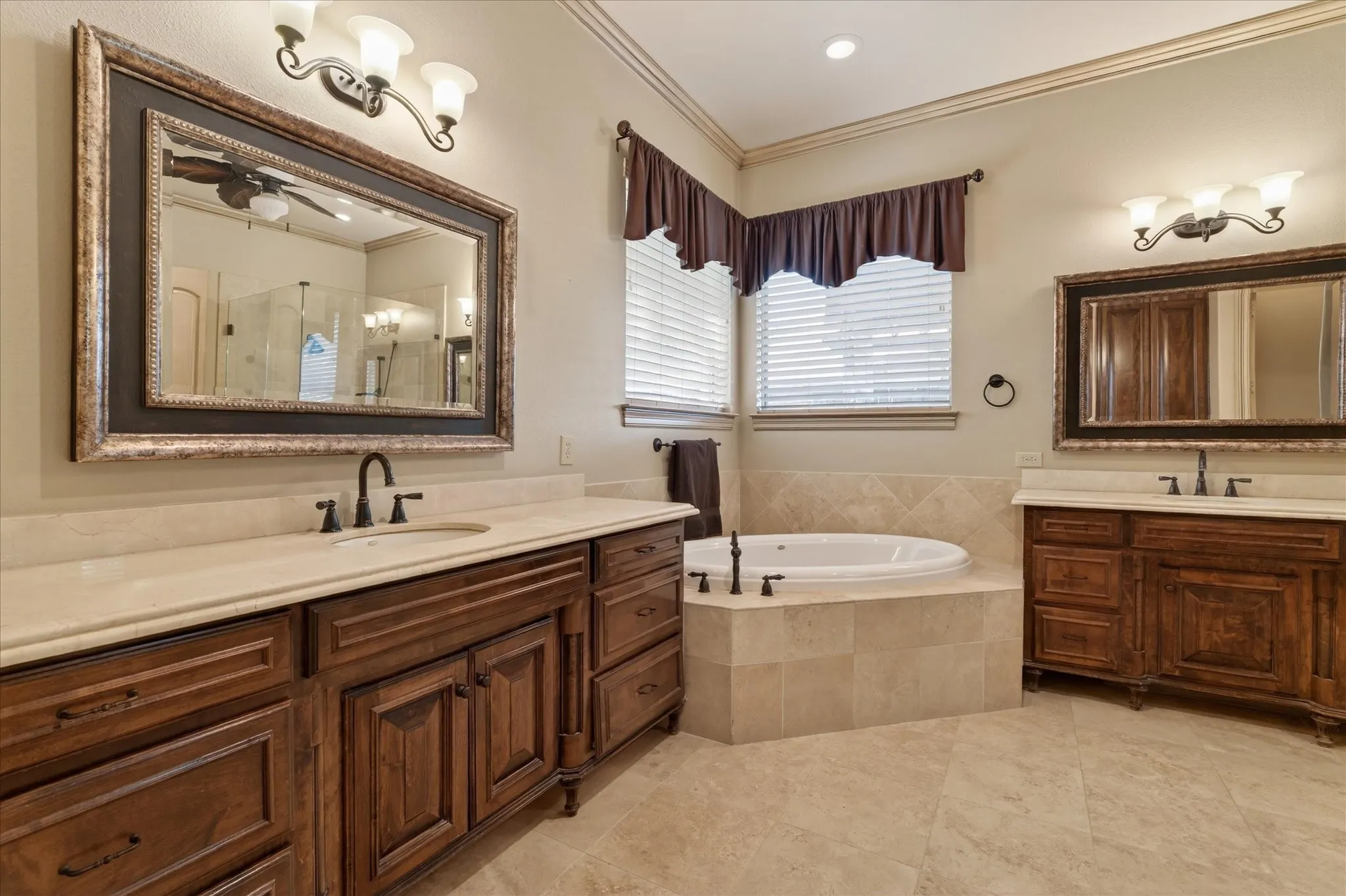 Bathroom featuring dual vanity areas with wood-finish cabinetry and light-toned countertops, a built-in jetted tub, and tiled flooring
