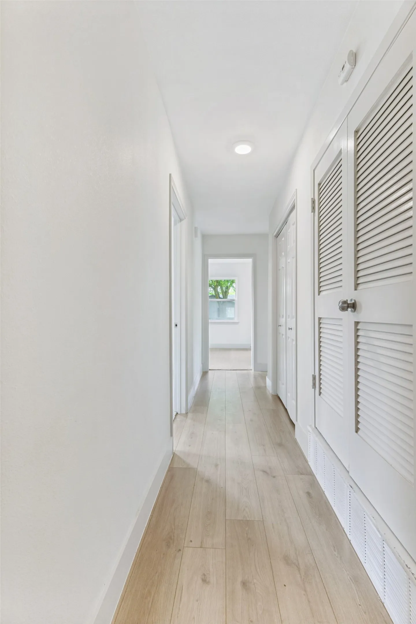 Bright hallway featuring light wood-finish flooring, white walls, and recessed lighting