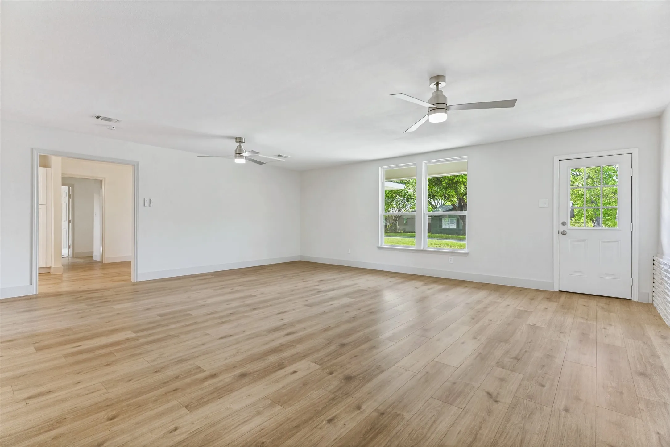 Spacious room featuring wood-finish flooring, crisp white walls, and multiple windows providing natural light