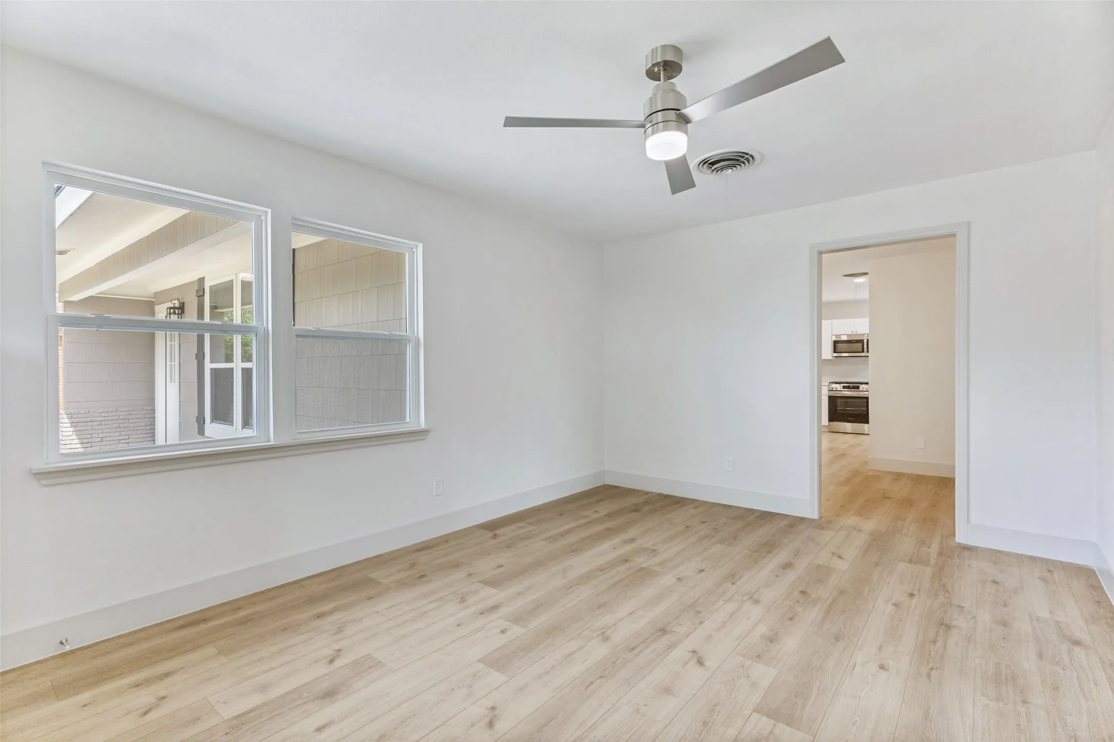 Bright interior space featuring light wood-finish flooring, white baseboards, and a modern ceiling fan with integrated lighting