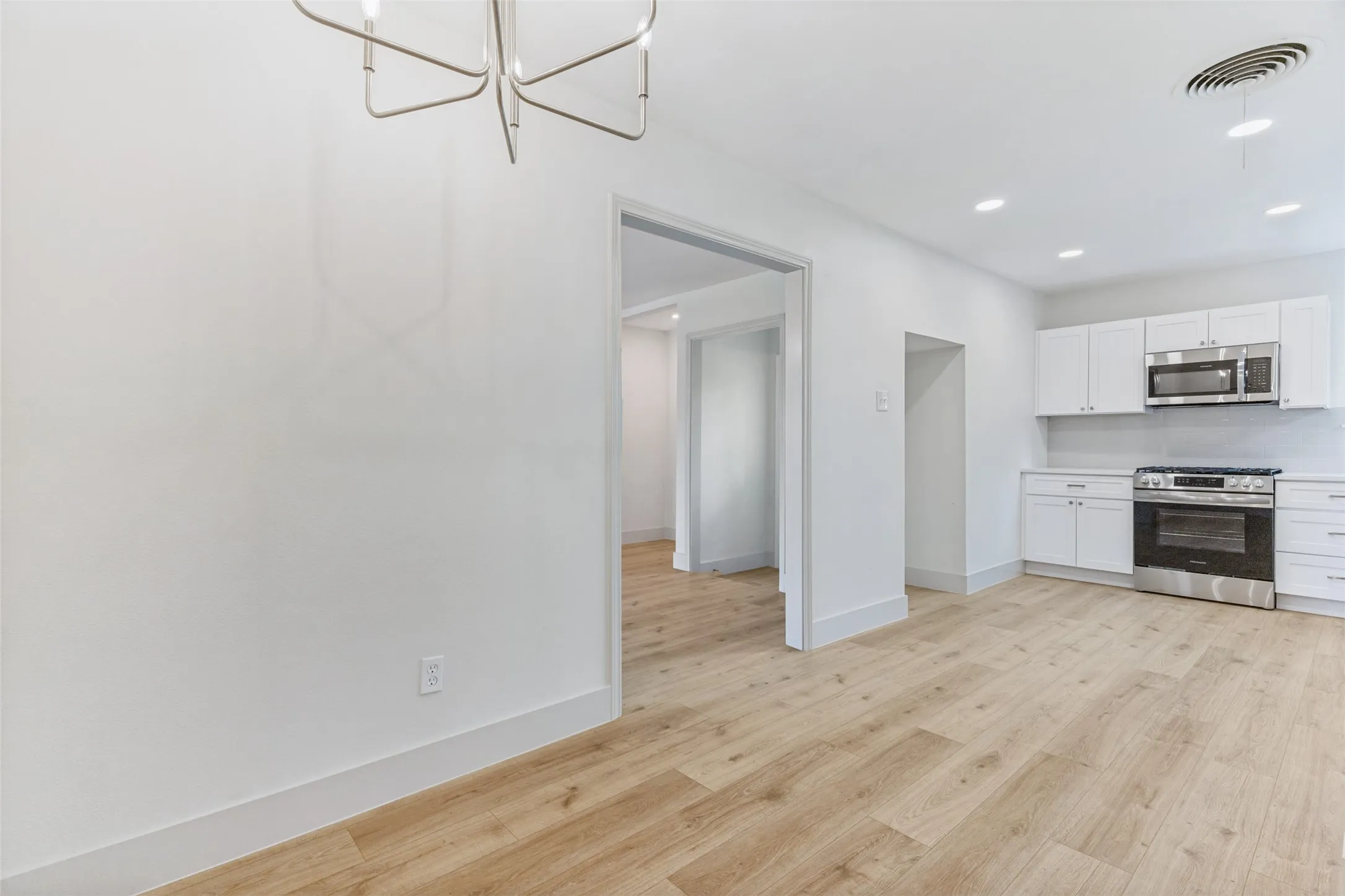 Open-concept living space featuring wood-finish flooring, recessed lighting, and a contemporary chandelier
