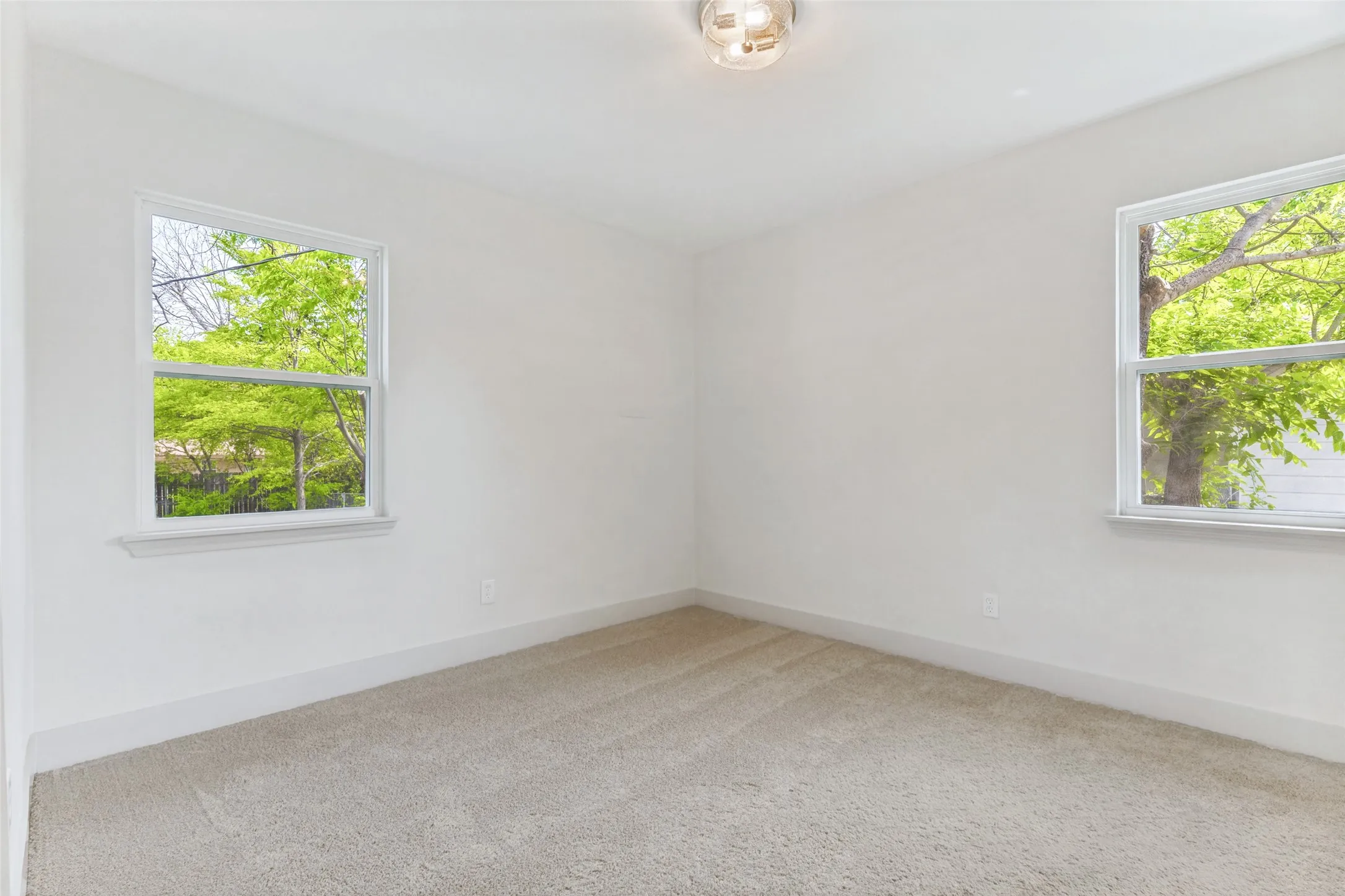 Carpeted room with white walls, two windows, and a flush mount light fixture