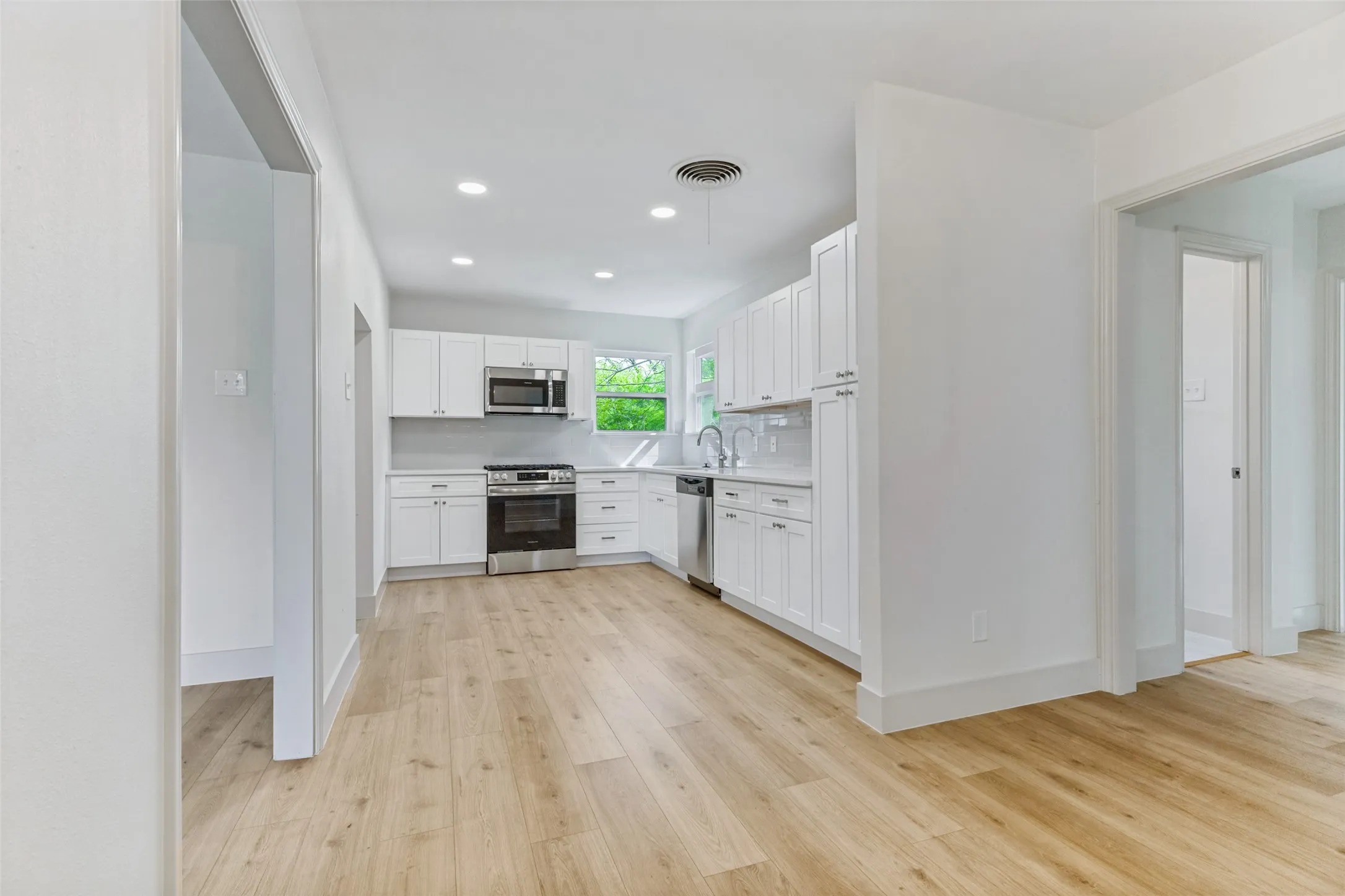 Kitchen featuring white shaker cabinetry, stainless steel appliances, light-toned wood-finish flooring, recessed lighting, and a window with exterior views