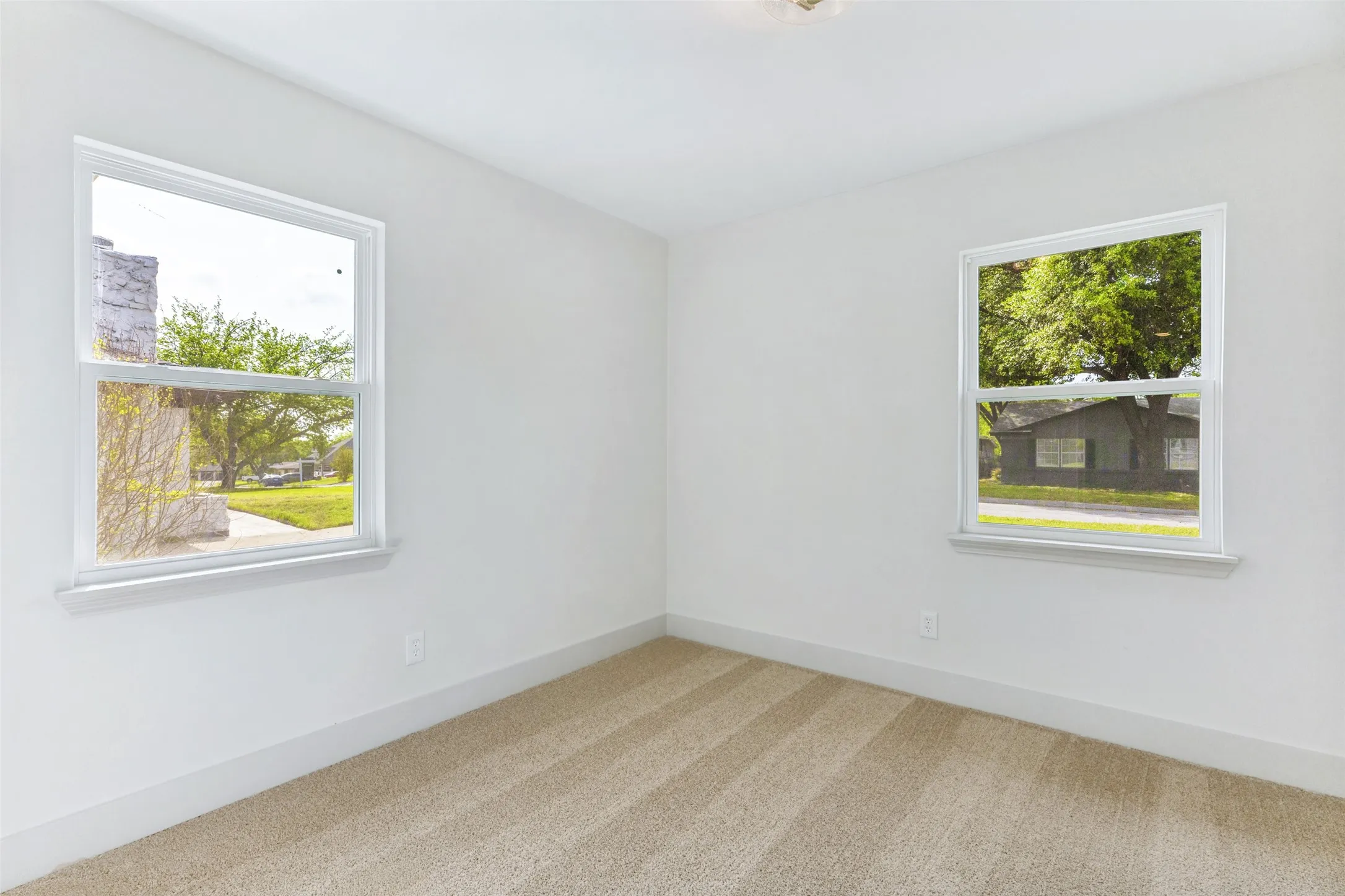 Room featuring two large windows, light beige striped carpet, white walls, and white baseboards