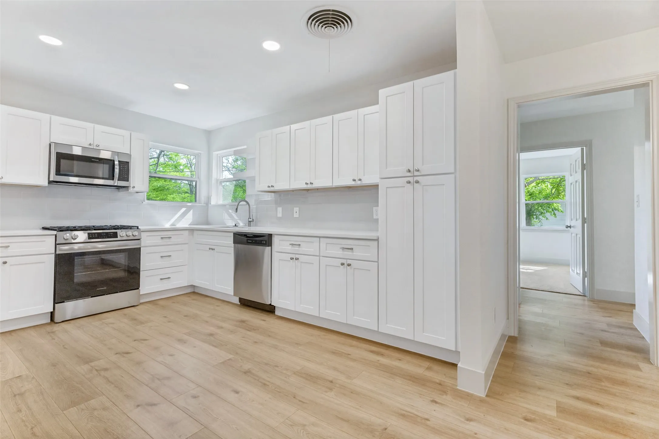 Kitchen featuring light wood-finish flooring, white shaker cabinetry, stainless steel appliances, a white tile backsplash, and a double window