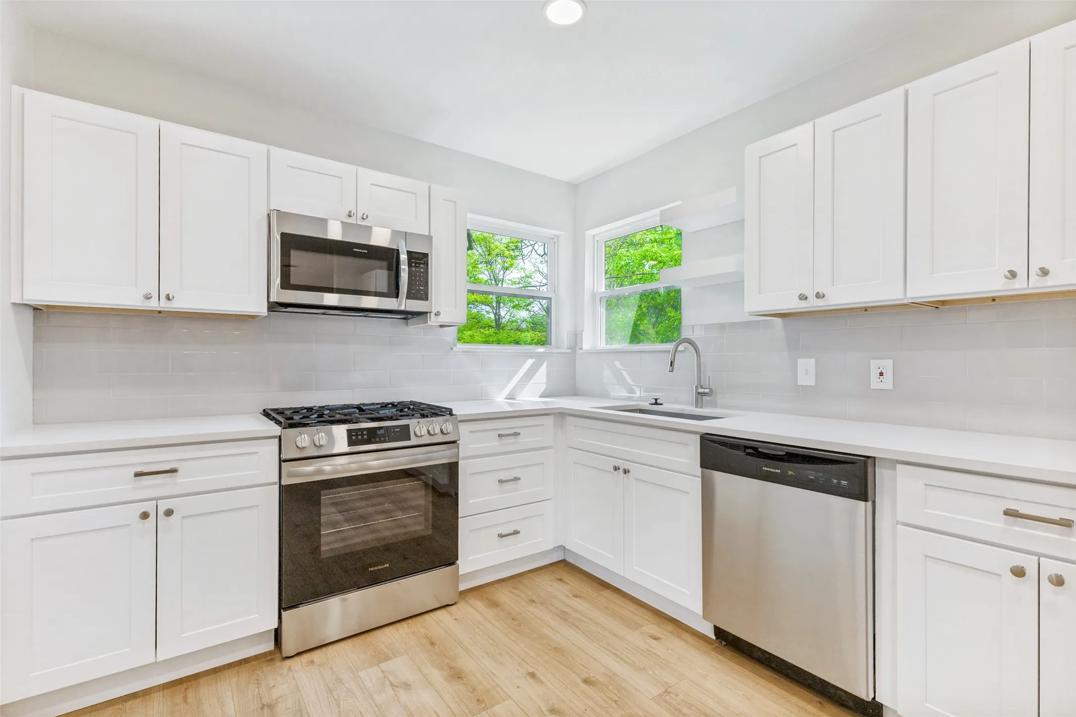 Modern kitchen featuring white shaker cabinetry, stainless steel appliances, light wood-finish flooring, white countertops, and a subway tile backsplash