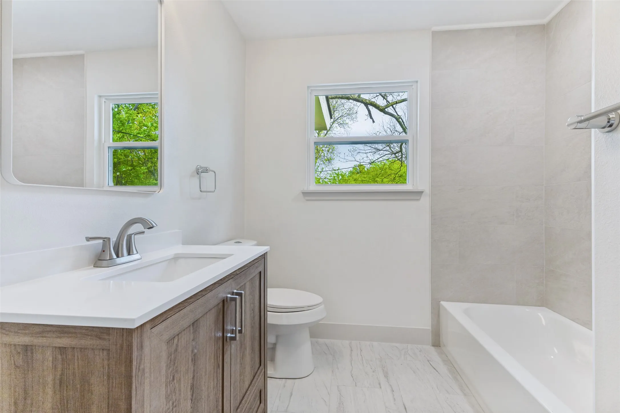 Bathroom featuring a wood-finish vanity with an integrated sink, a white countertop, and a contemporary faucet