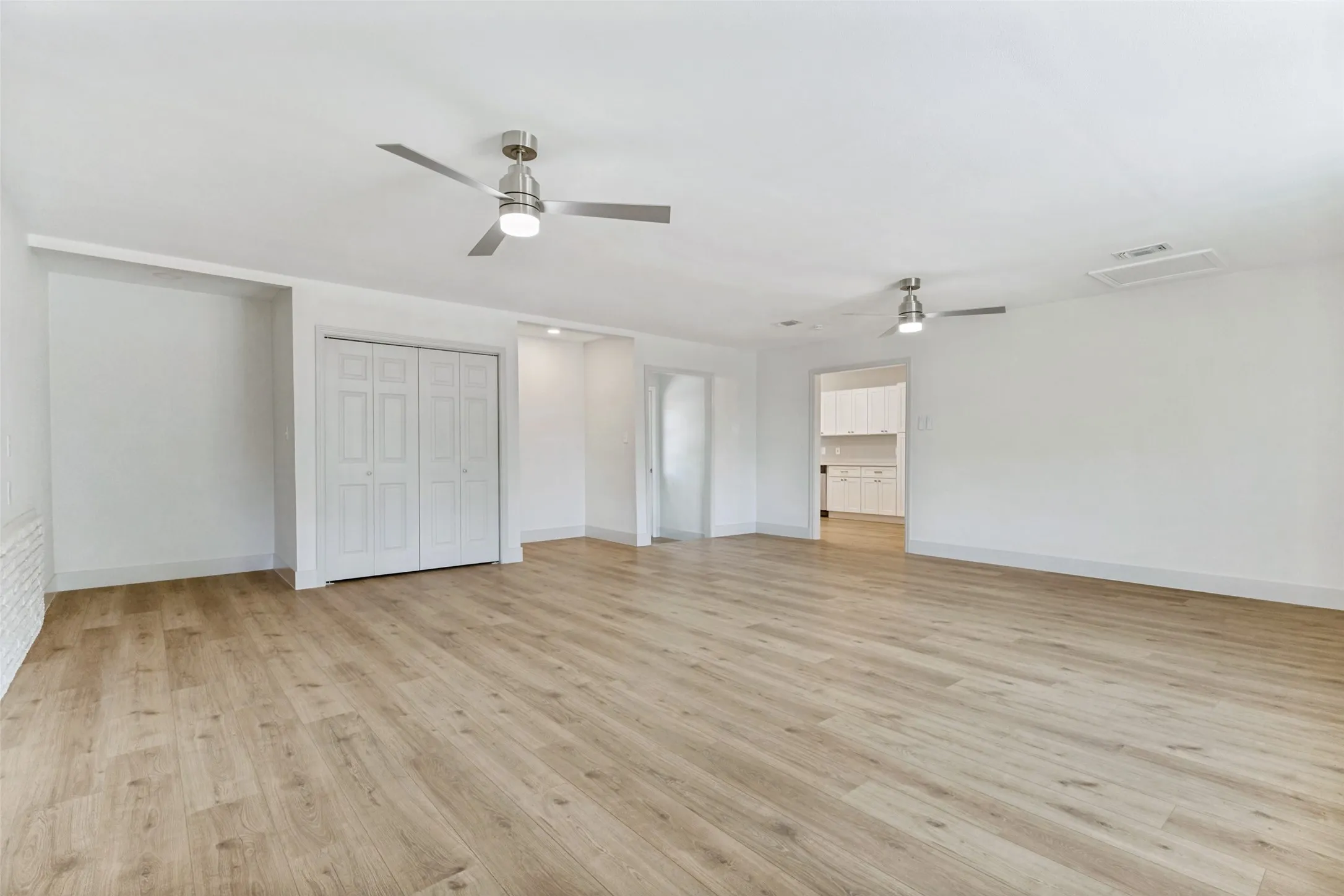 Spacious room featuring wood-finish flooring, two ceiling fans with integrated lighting, white bi-fold closet doors, and recessed wall shelving