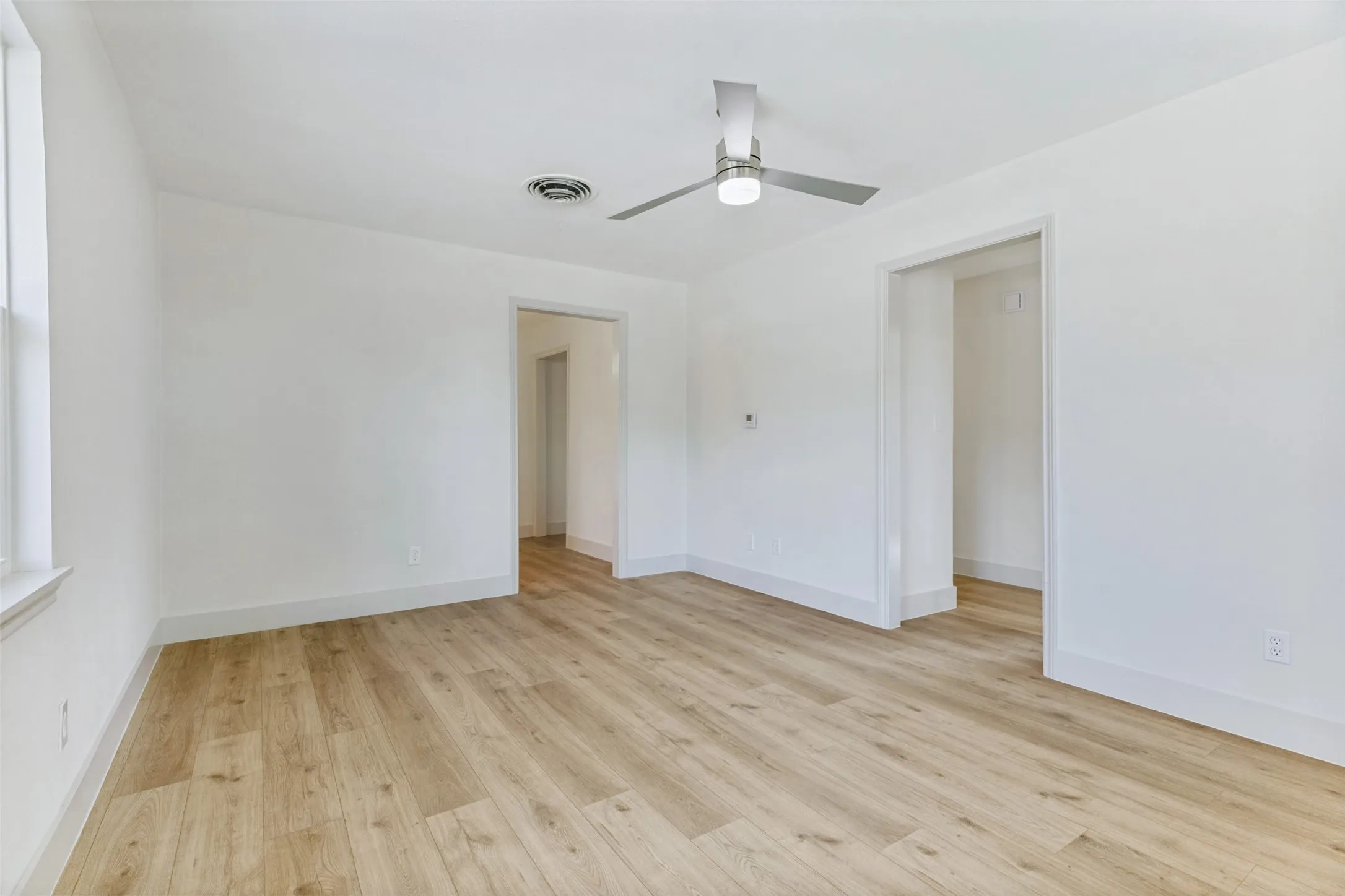 Bright interior space featuring light wood-finish flooring, white walls, and a contemporary ceiling fan with integrated lighting