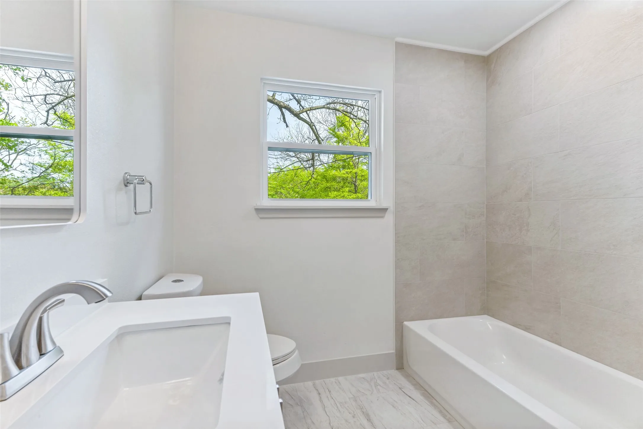 Bathroom featuring a white vanity with integrated sink, brushed nickel faucet, light-toned wall tiling in the shower area, and a white bathtub