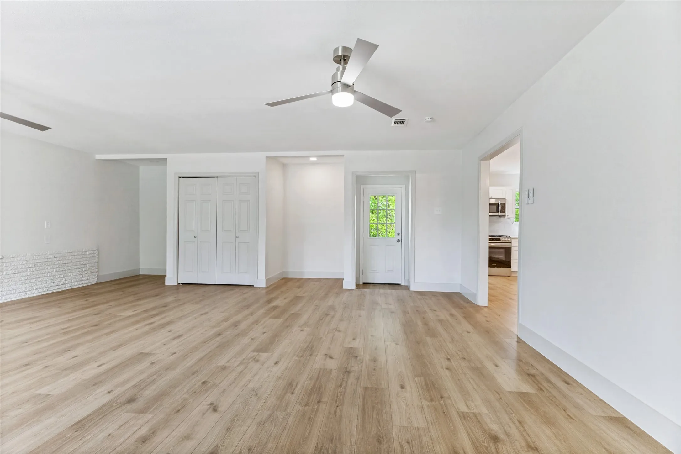 Spacious room featuring wood-finish flooring, white walls, and a contemporary ceiling fan with integrated lighting